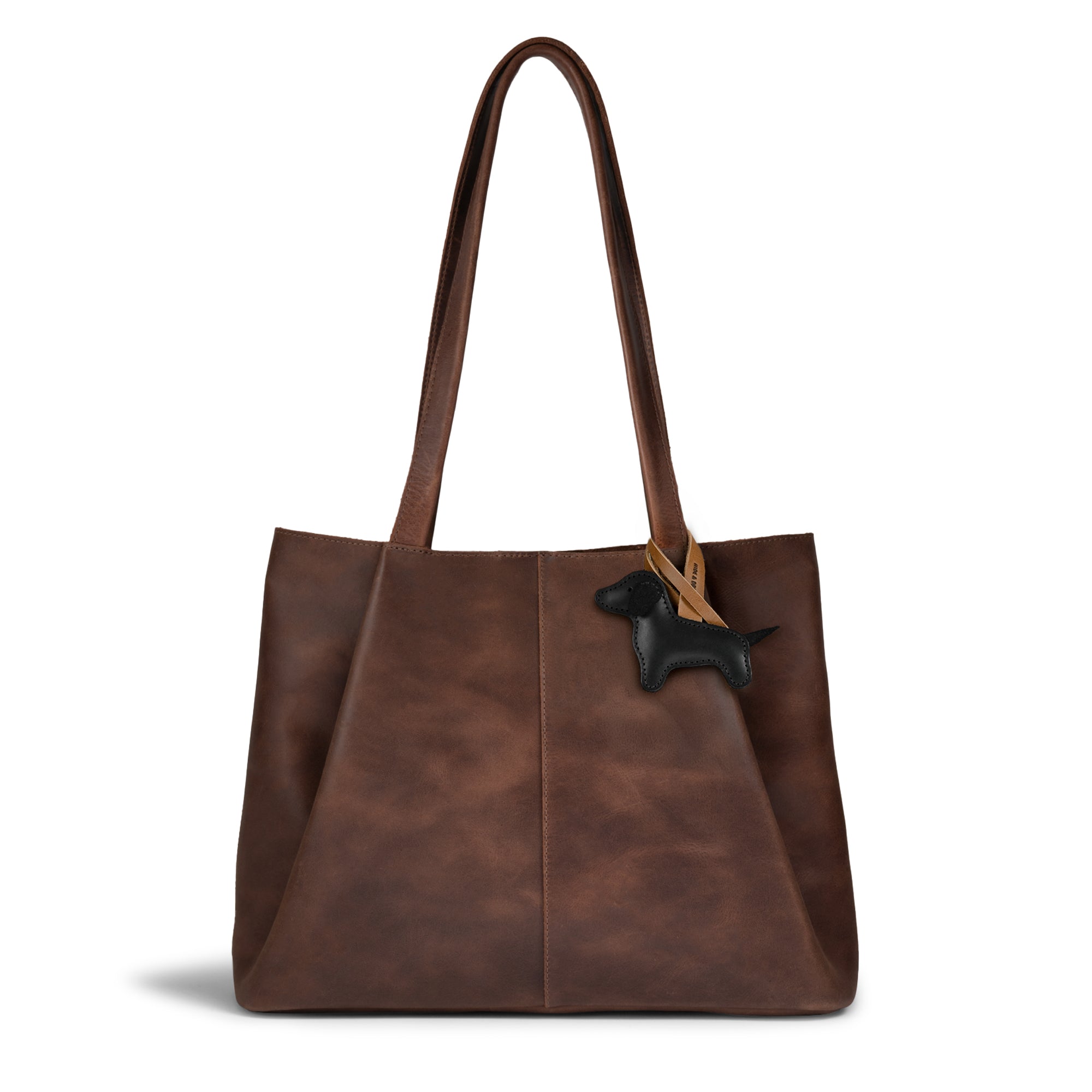 Dachshund Bag Charm from Hide & Drink attached to a chic brown tote bag. This full grain leather dog charm adds a unique touch, making it an ideal ornament for women’s handbags, purses, and backpacks. Hand cut and hand sewn with fire branded detailing, this charming piece is a statement of artisan craftsmanship, handmade in La Antigua, Guatemala and Oaxaca, Mexico.