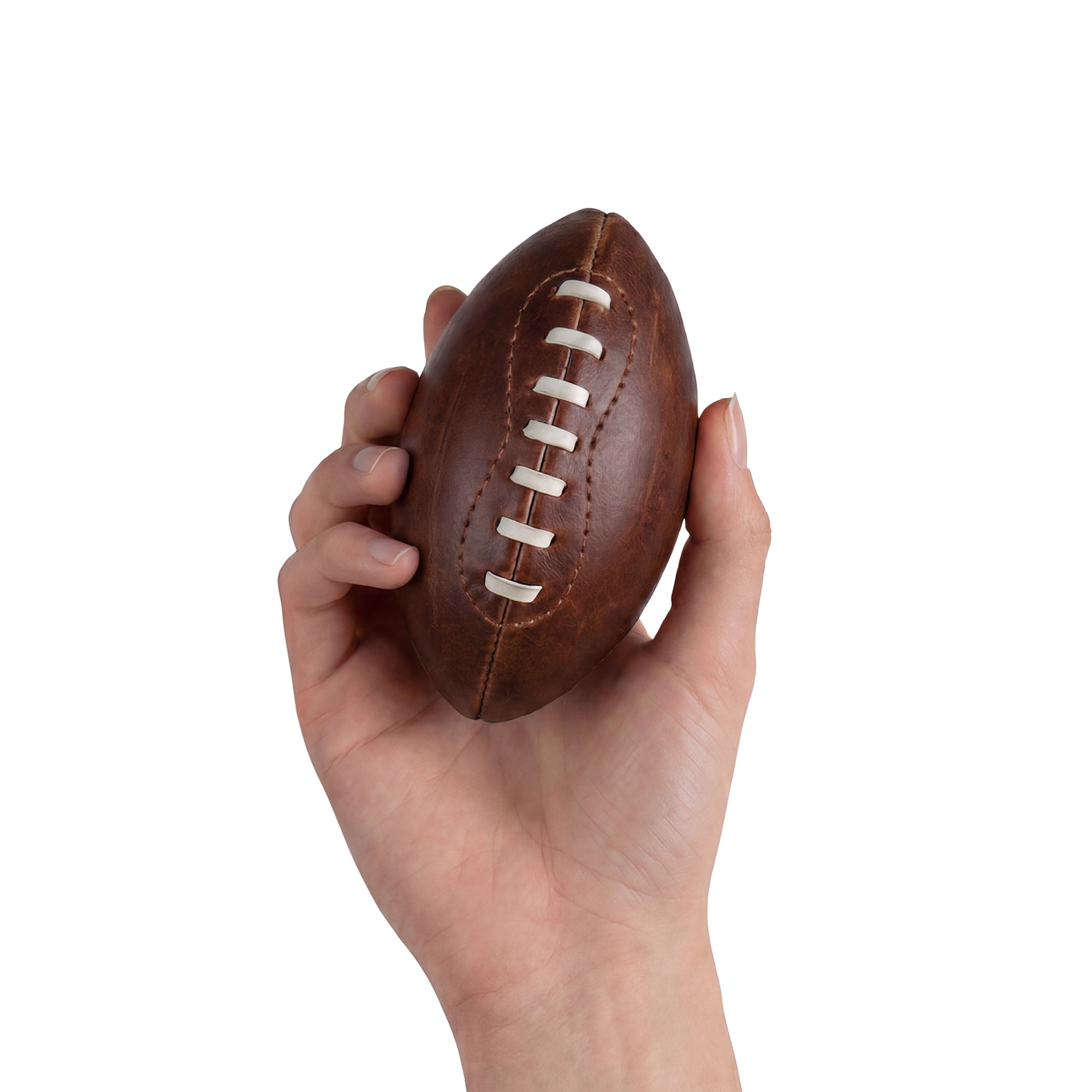 A hand holding a Mini American Football by Hide & Drink, demonstrating its small size and fine craftsmanship. This hand cut ball, made from full grain leather, makes for an excellent keepsake or display item, showcasing the brand's dedication to artisanal production.