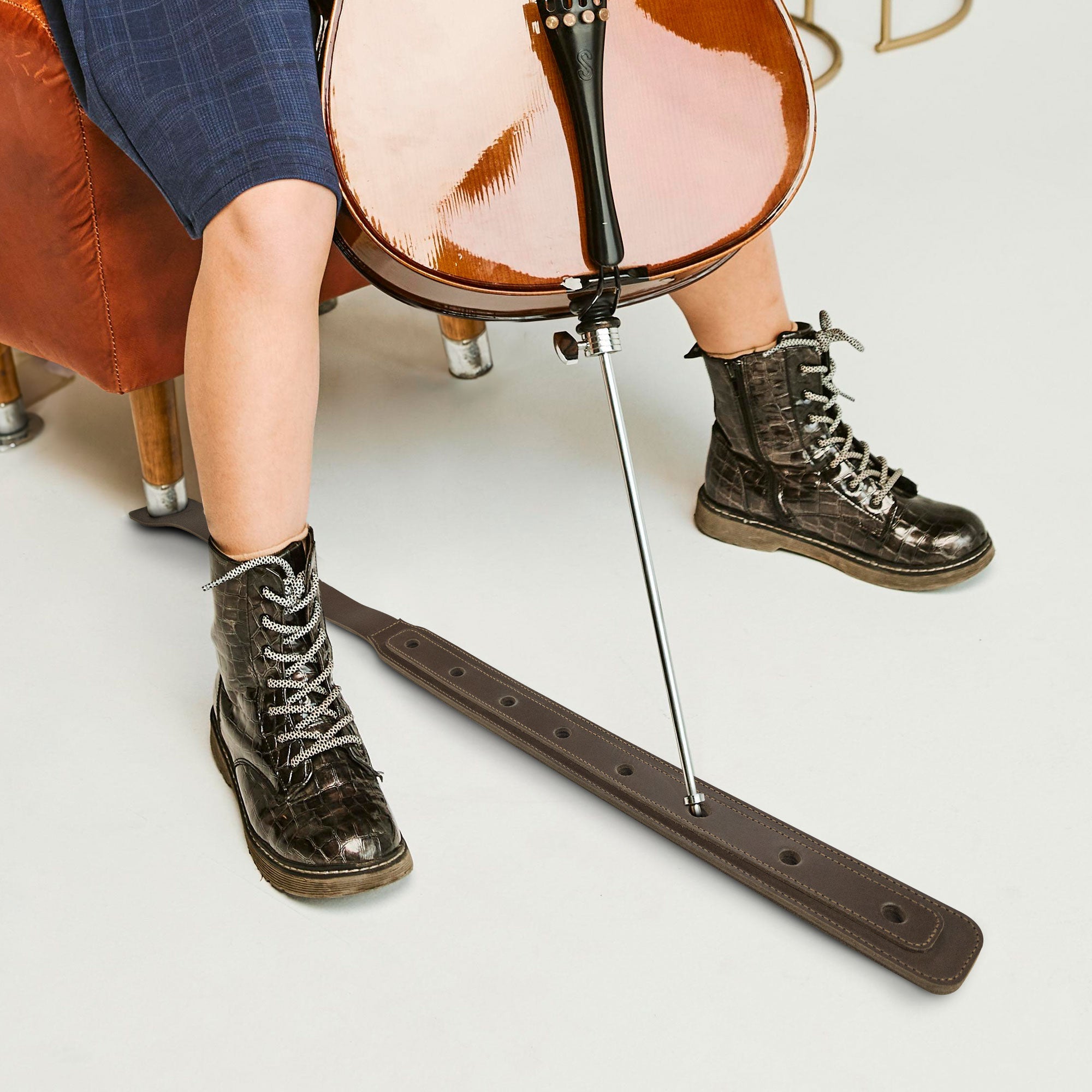 A Cello Endpin Strap Stopper in action, shown with a cello and a musician‚Äôs stylish boots. This Classic Non-Slip Stopper by tocame ensures stability and protects floors while practicing. Made from durable full grain leather, this artisan accessory exemplifies small batch production and handcrafted excellence.