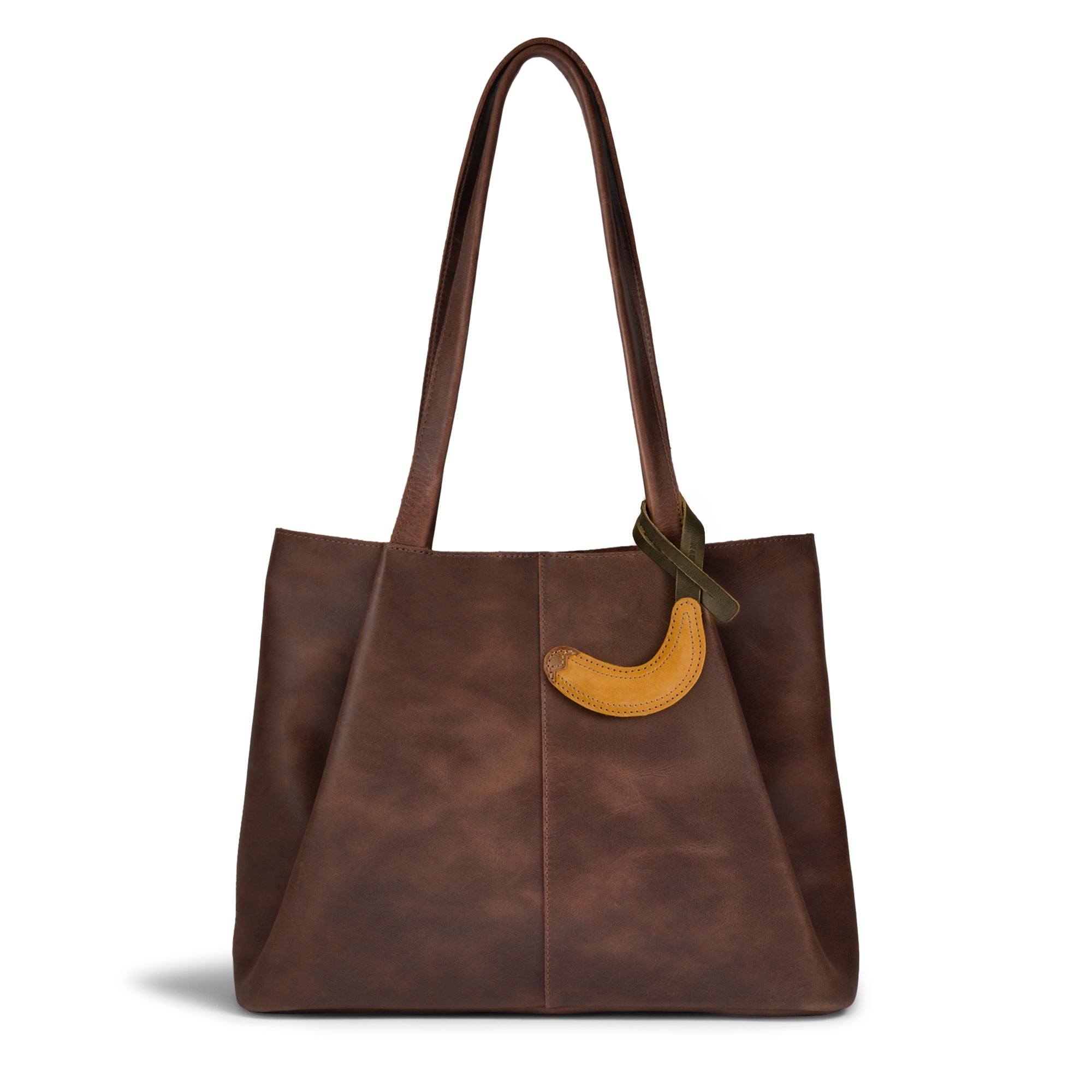 Hide & Drink Banana Bag Charm attached to a stylish brown tote bag. This accessory elevates your look and is ideal as a purse charm for totes and backpacks. Crafted from full grain leather, it's truly an ornament for women that reflects handmade quality from La Antigua Guatemala and Oaxaca Mexico, emphasizing small batch production and artisan craftsmanship.