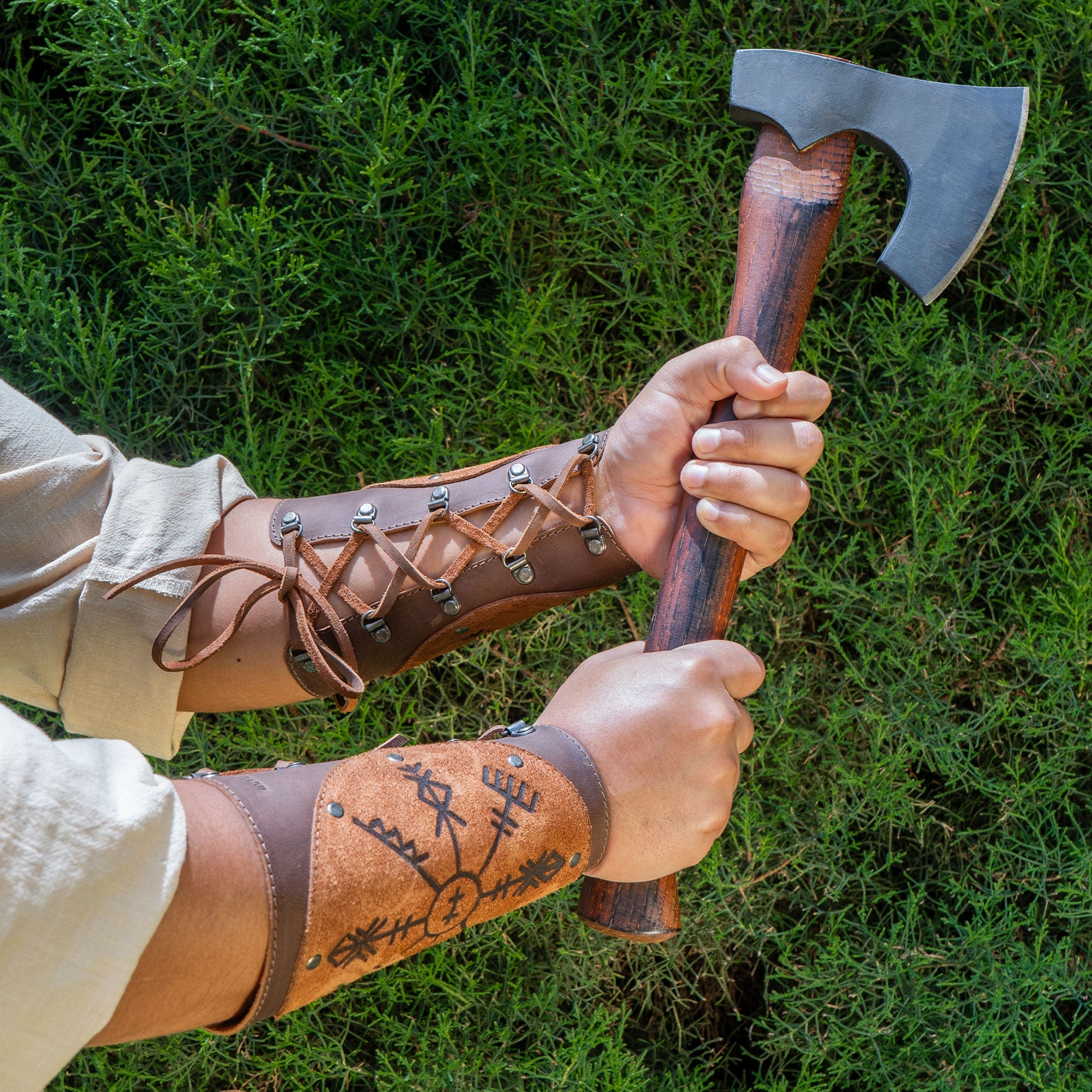 A model wearing Viking Bracers by Hide & Play while holding an axe, highlighting the impressive features of this set of 2 Viking Style Bracers. These arm protectors for costume are made from full grain leather, ideal for cosplay, featuring small batch production and artisanal craftsmanship from La Antigua Guatemala & Oaxaca Mexico.