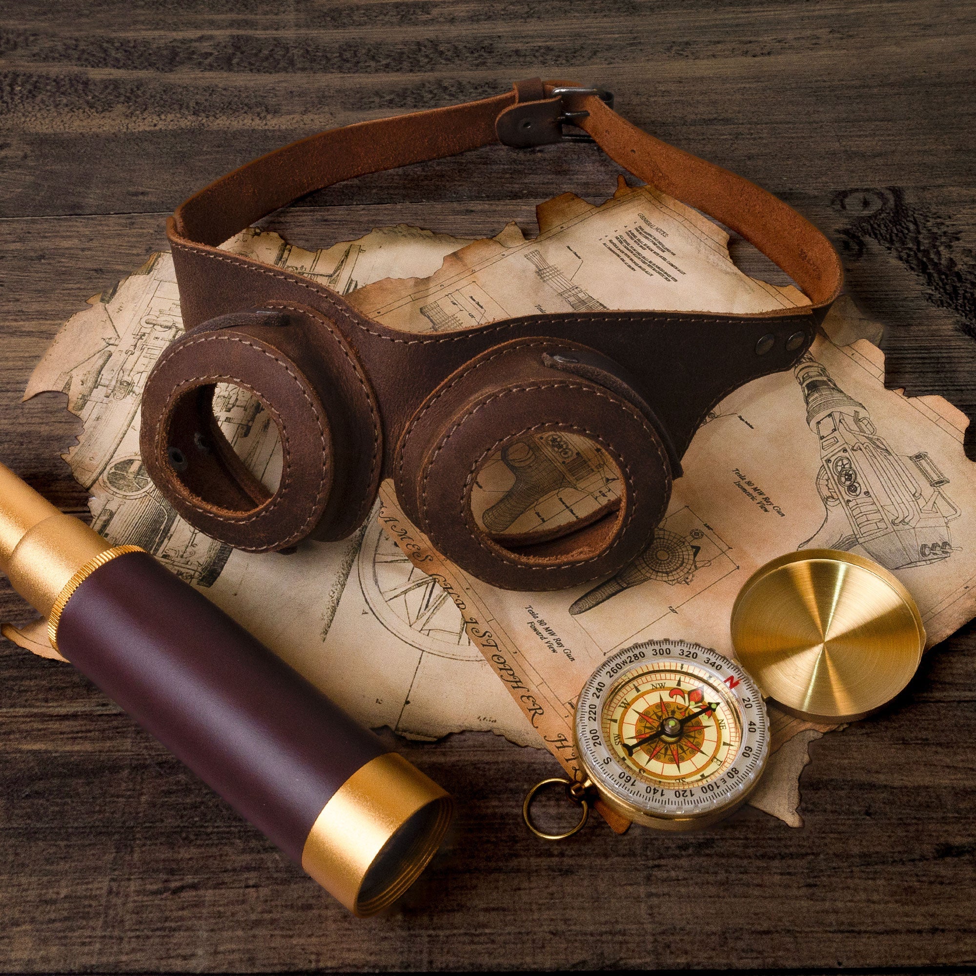 The Steampunk Style Goggles by Hide & Play, surrounded by vintage themed items like a compass and telescope. This retro cosplay prop highlights the craftsmanship of full grain leather, making it an excellent accessory for any costume. Hand cut and hand sewn in small batches by artisans in La Antigua Guatemala & Oaxaca Mexico.