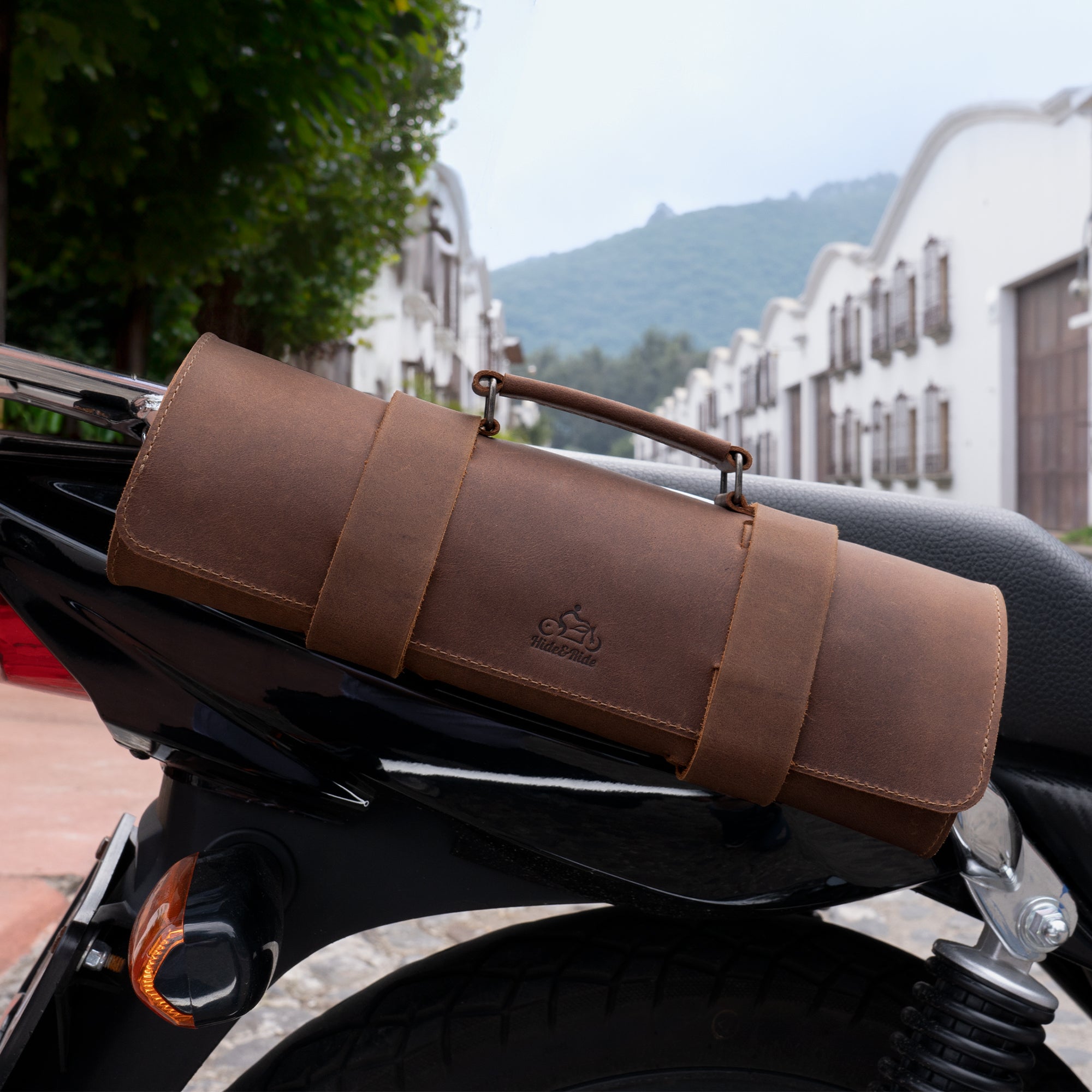 Tool Roll for Bikers displayed on a motorcycle seat, showcasing the stylish brown leather design by Hide & Ride. This Motorcycle Tool Bag doubles as a Universal Saddlebag for Motorcycle and Fork Bag for Bikers, emphasizing exquisite Full Grain Leather craftsmanship. Discover the quality of Small Batch Production with Hand Cut and Hand Sewn finishes, made by talented artisans in La Antigua Guatemala & Oaxaca Mexico.