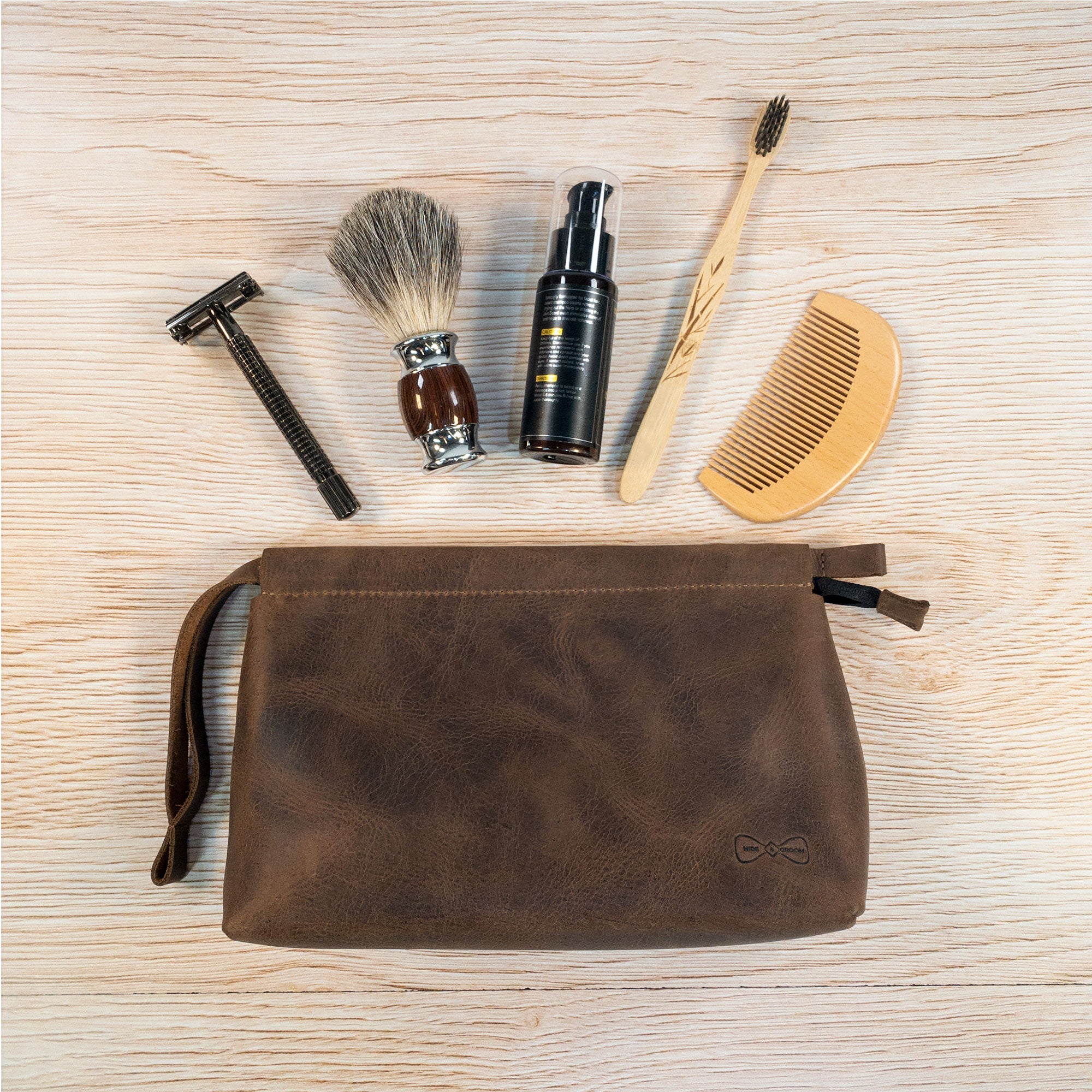 The Rectangular Toiletry Bag with Sliding Handle for Groomsmen by Hide & Groom is shown alongside grooming essentials, showcasing its functionality for best men and living up to its reputation as a shaving kit storage bag. Its full grain leather design highlights artisan craftsmanship and is handmade in La Antigua Guatemala.
