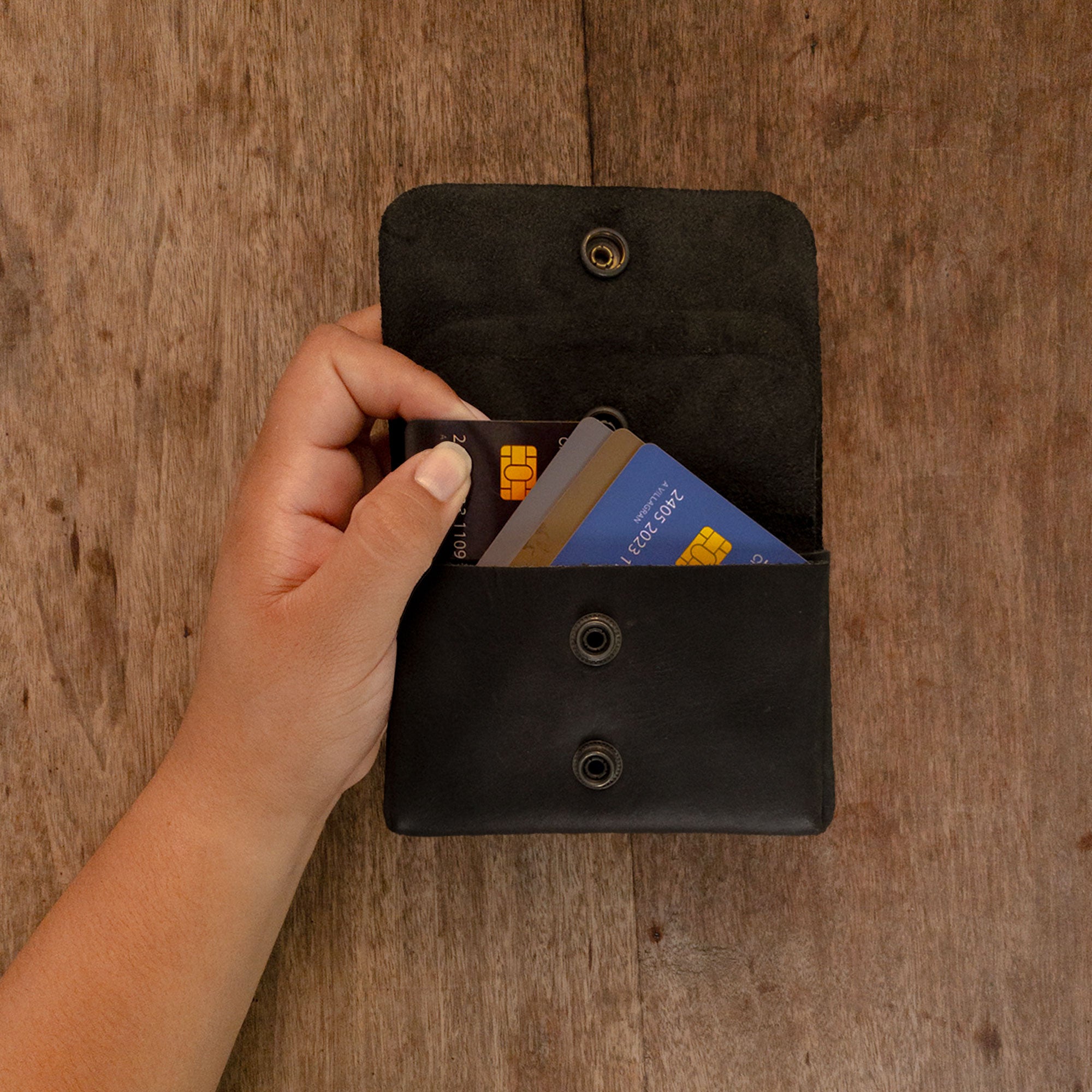 A hand using the black Double Pouch Card Wallet by Hide & Drink to pull out cards. This Leather Double Pouch Card Wallet doubles as a handy card organizer, cash holder, and coin pouch, ideal for both men and women. Full Grain Leather, handcrafted in La Antigua Guatemala & Oaxaca Mexico.