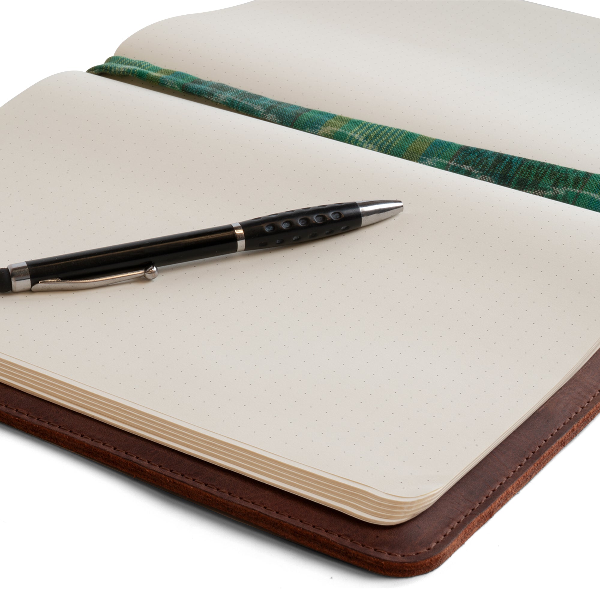 Close-up of the Full Grain Leather Journal Cover for Moleskine Cahier XL (7.5 x 9.75 in.) by Hide & Drink featuring a pen resting on the open pages. This richly textured notebook case enhances your writing experience while showcasing hand sewn techniques, small batch production, and dedication to craftsmanship from La Antigua Guatemala & Oaxaca Mexico.
