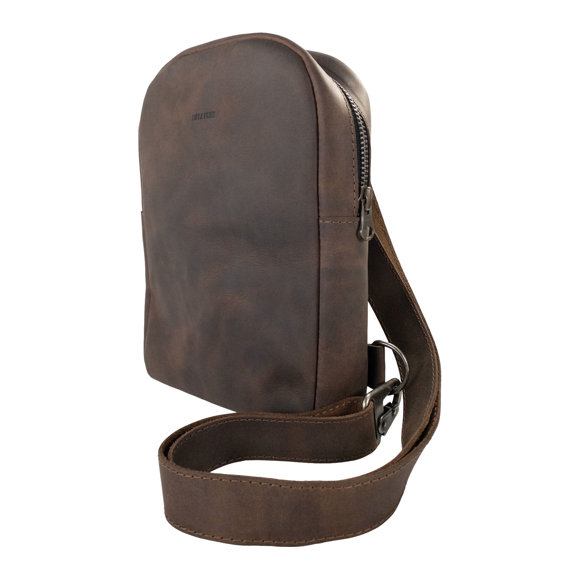 Side view of the Hide & Drink Crossbody Rounded Bag, highlighting its sleek design. This Rounded Crossbody Bag with Adjustable Strap is a reliable messenger bag made from premium Full Grain Leather, featuring small batch production techniques and artisan craftsmanship from La Antigua Guatemala & Oaxaca Mexico.