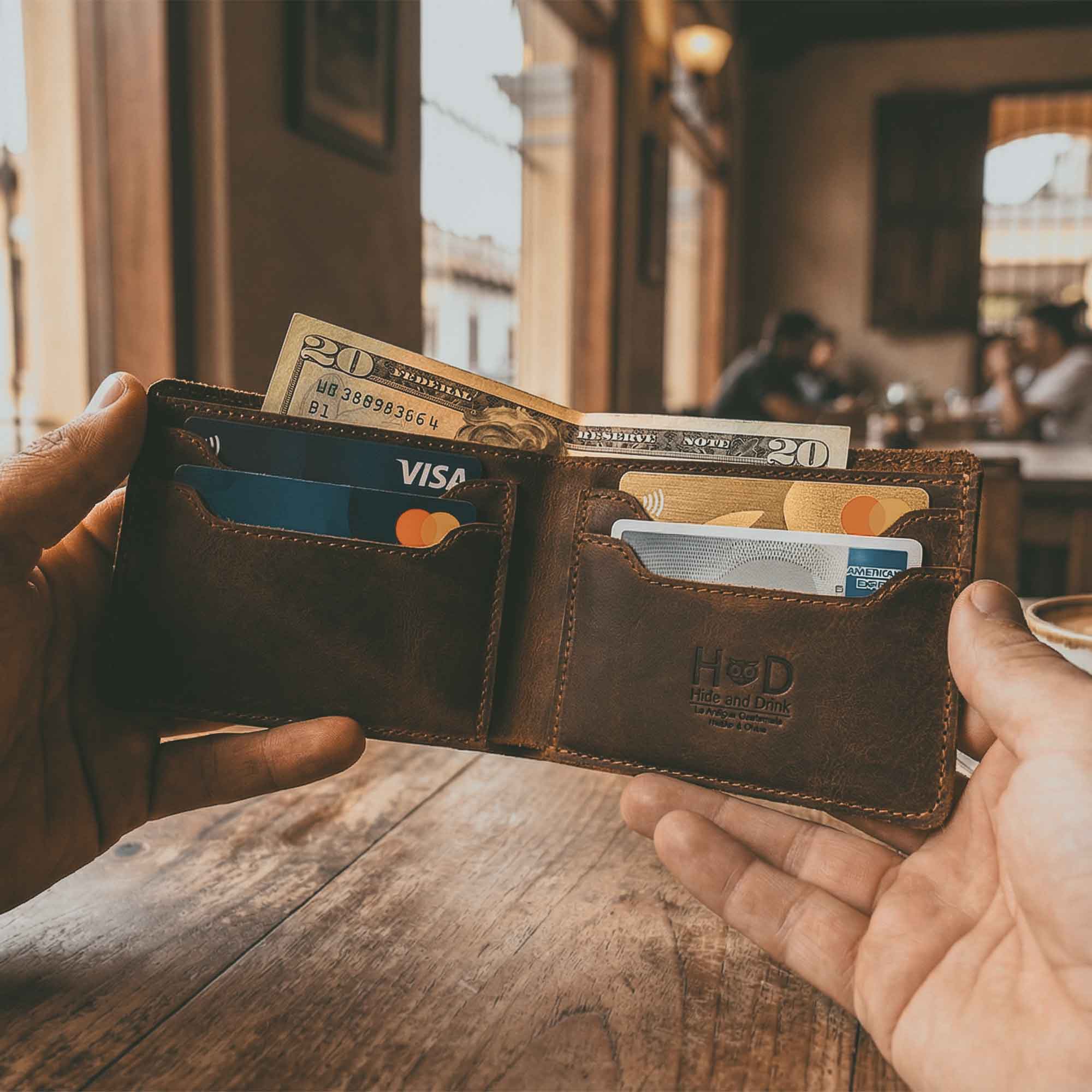Classic Wallet by Hide & Drink displayed open and filled with cash and cards. This Classic Bifold Wallet, crafted from Full Grain Leather, features multiple card slots for convenience, making it an ideal storage case for identification. A stylish travel accessory, it represents artisan small batch production, hand cut and sewn in La Antigua Guatemala & Oaxaca Mexico.