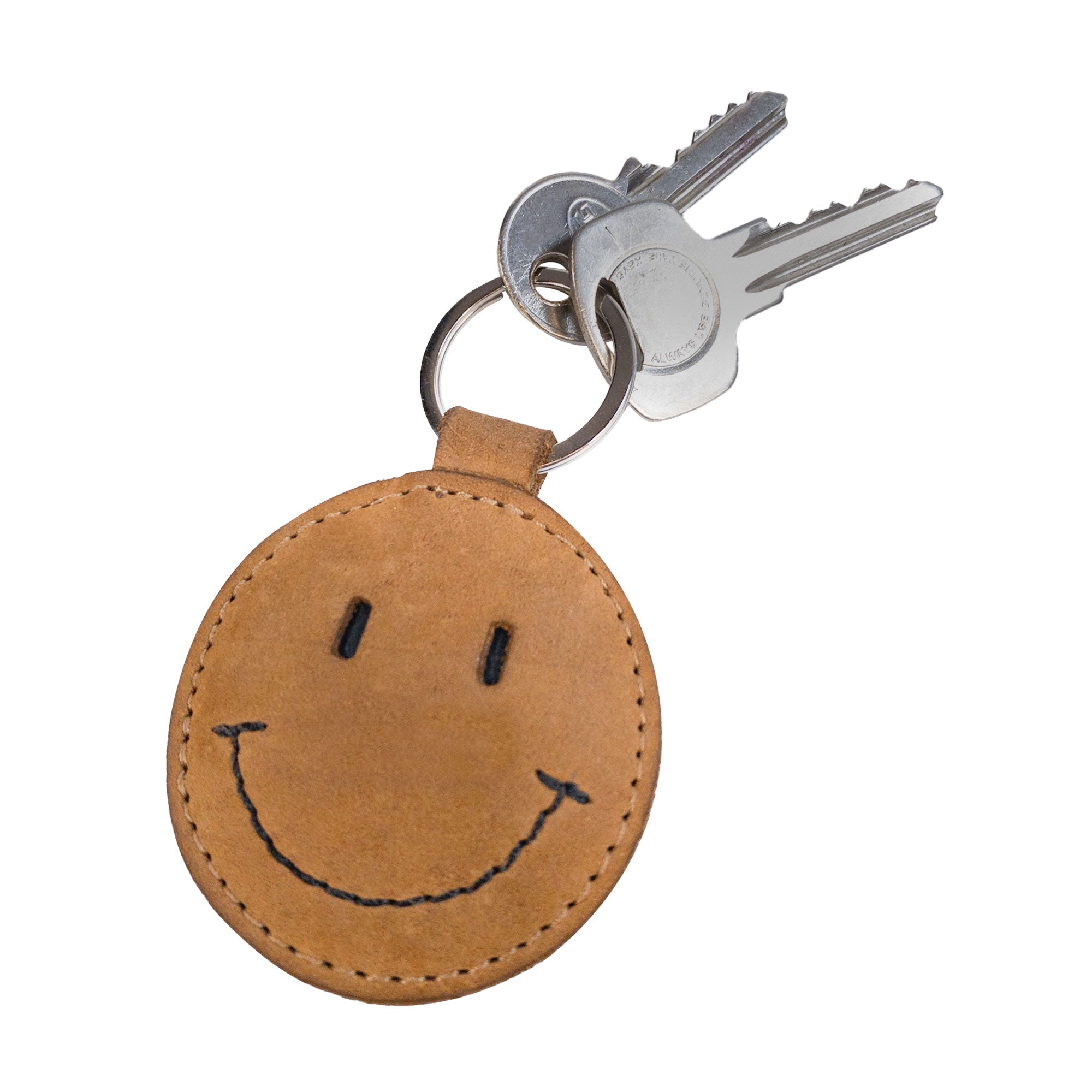 An angled view of the Smiley Face Keychain by Hide & Drink, demonstrating its charming smile design attached to a set of keys. This key holder is crafted with Full Grain Leather for durability and style, making it a delightful gift for anyone. A true artisan piece made in La Antigua Guatemala, perfect for casual accessories.