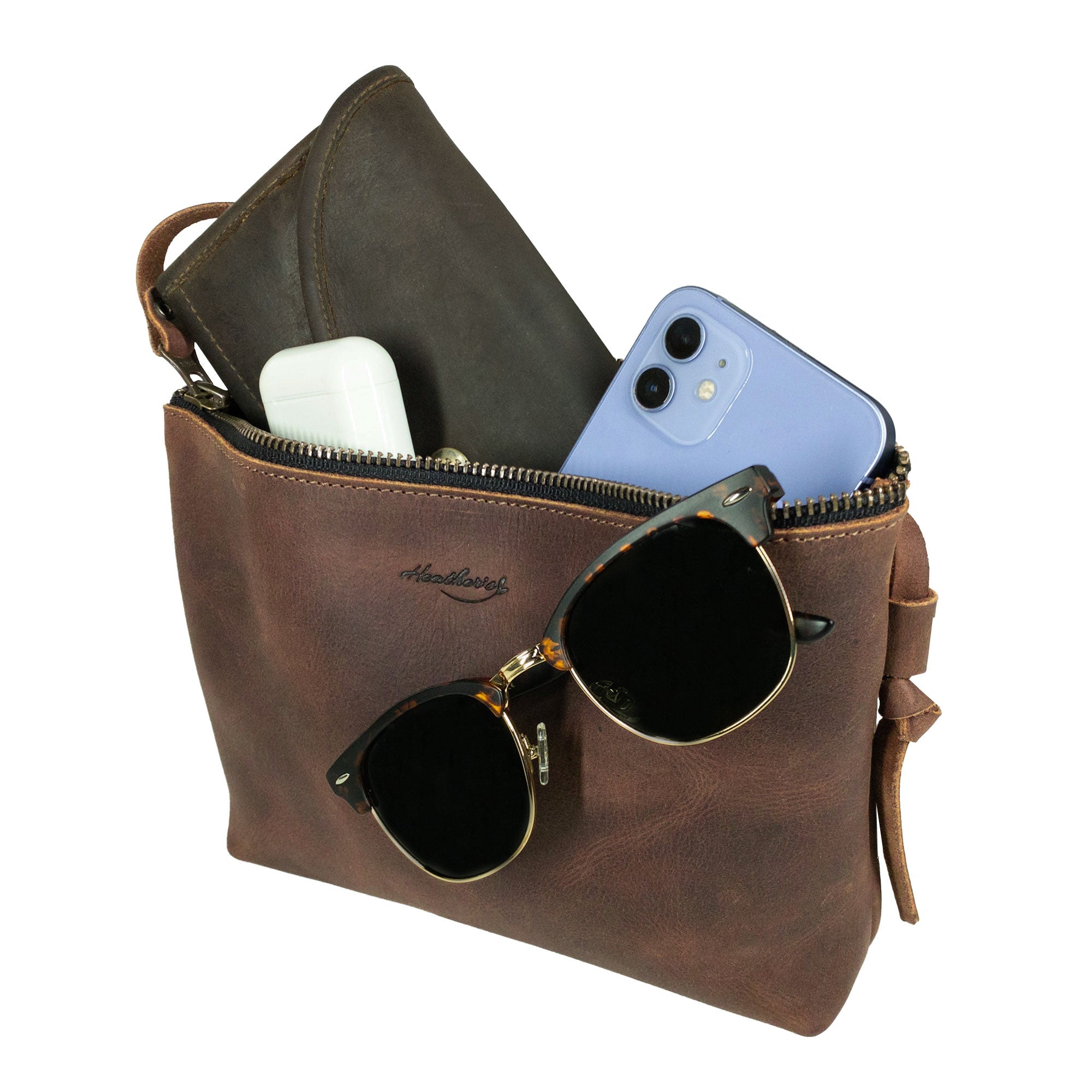 Heather's Clutch Bag with Strap styled with sunglasses and a phone, showcasing its versatility. This Full Grain Leather clutch serves as a wrist wallet for cards and money, perfect for makeup, cosmetics, and toiletry items, hand crafted in La Antigua Guatemala & Oaxaca Mexico.