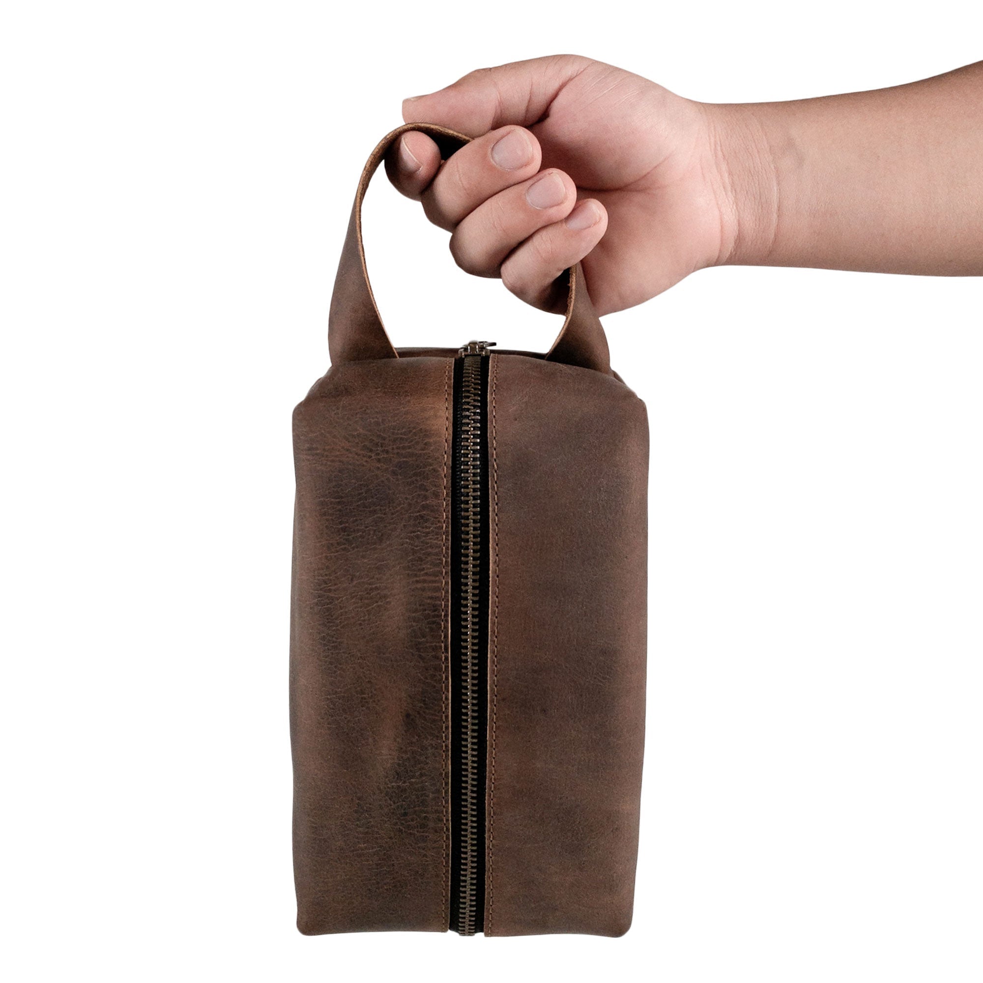 A hand holding Hide & Groom's rustic toiletry bag for groomsmen, highlighting its practical design and sturdy handle. This full grain leather bag is perfect for bachelors, providing stylish storage for grooming kits and showcasing craftsmanship from La Antigua Guatemala.