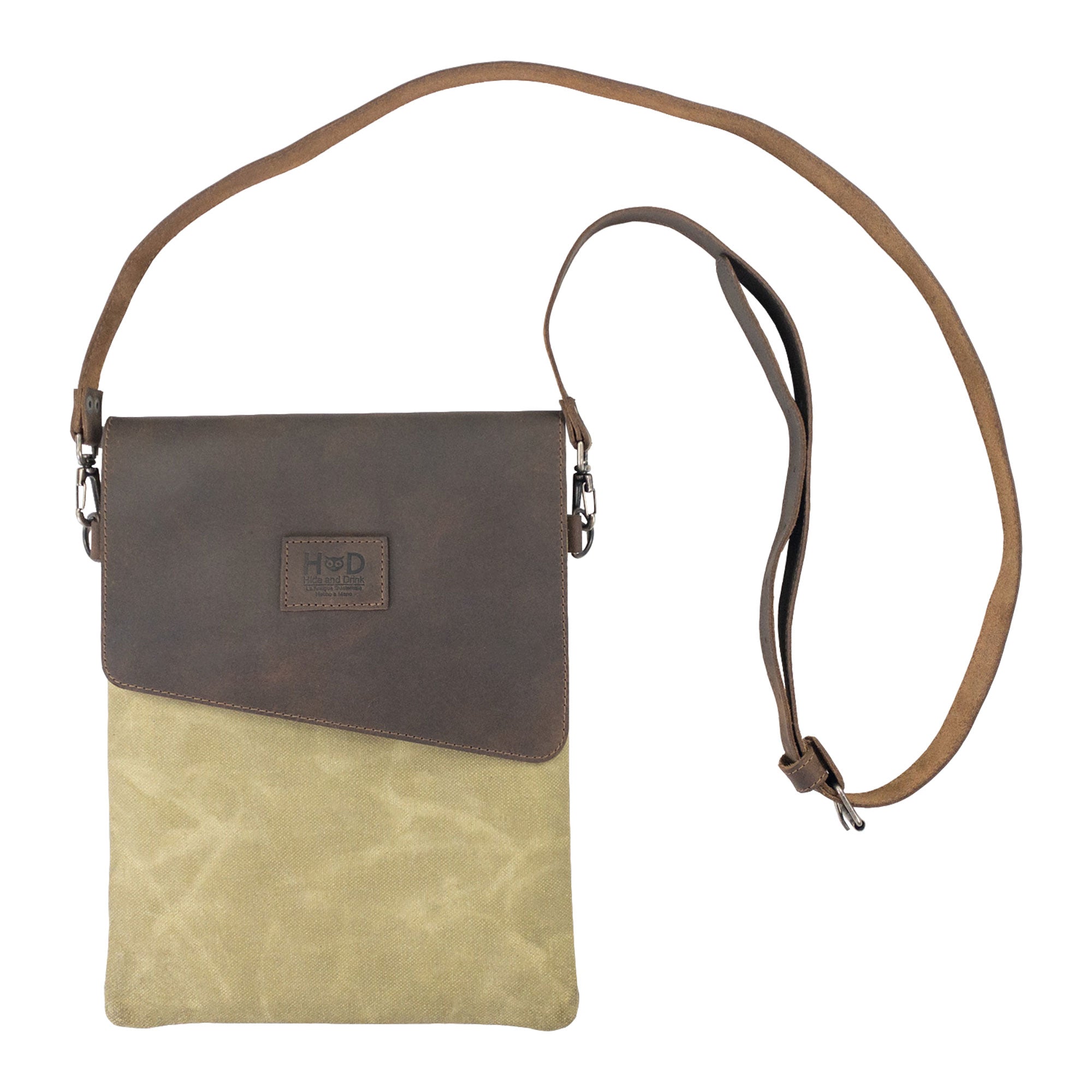 Hide & Drink Crossbody Bag resting on a flat surface, showing off its unique two-tone materials. This Crossbody Bag with Adjustable Shoulder Strap is a Unisex Messenger Bag made of fine Full Grain Leather & Waxed Canvas, featuring small batch production, hand cut, hand sewn, fire branded craftsmanship by artisans in La Antigua Guatemala & Oaxaca Mexico.