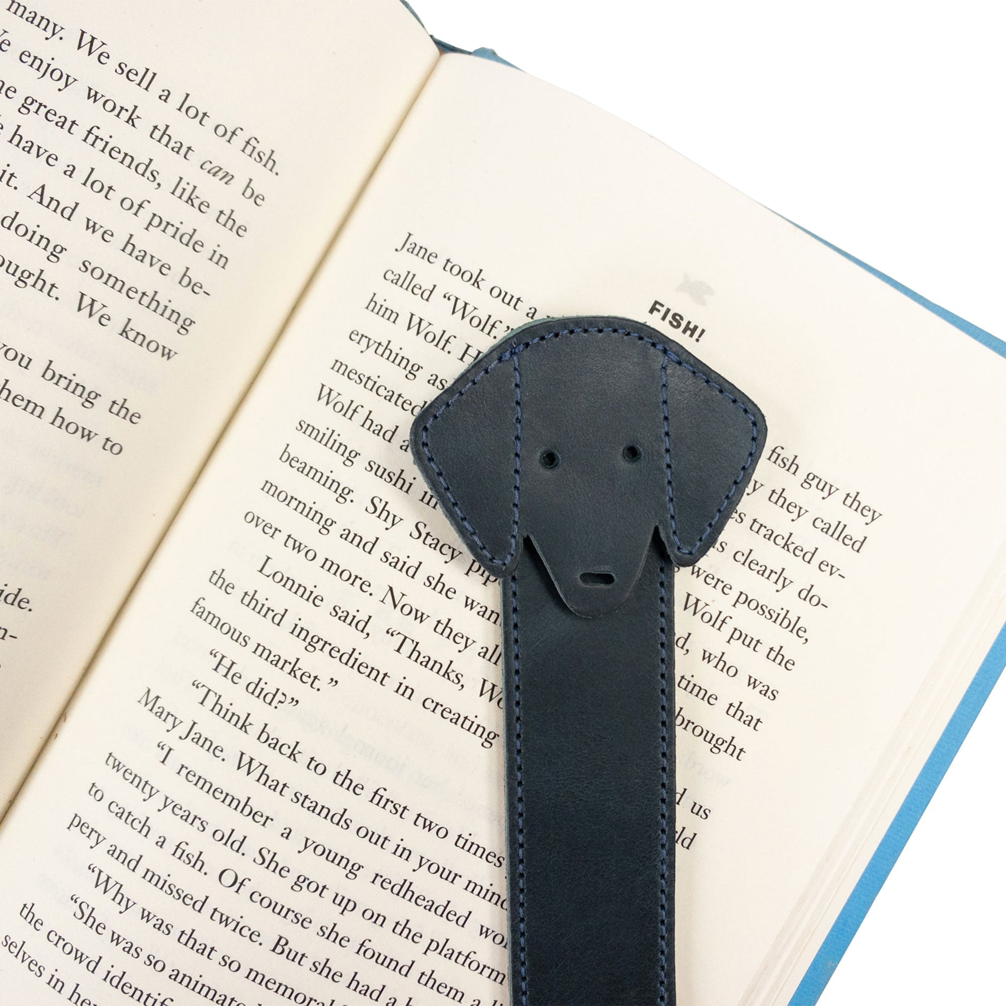 Close-up of Hide & Drink's navy Dog Bookmark resting on a book page, emphasizing its Full Grain Leather quality. This artisan bookmark reflects small batch production and fire branding efforts, crafted in La Antigua Guatemala & Oaxaca Mexico.
