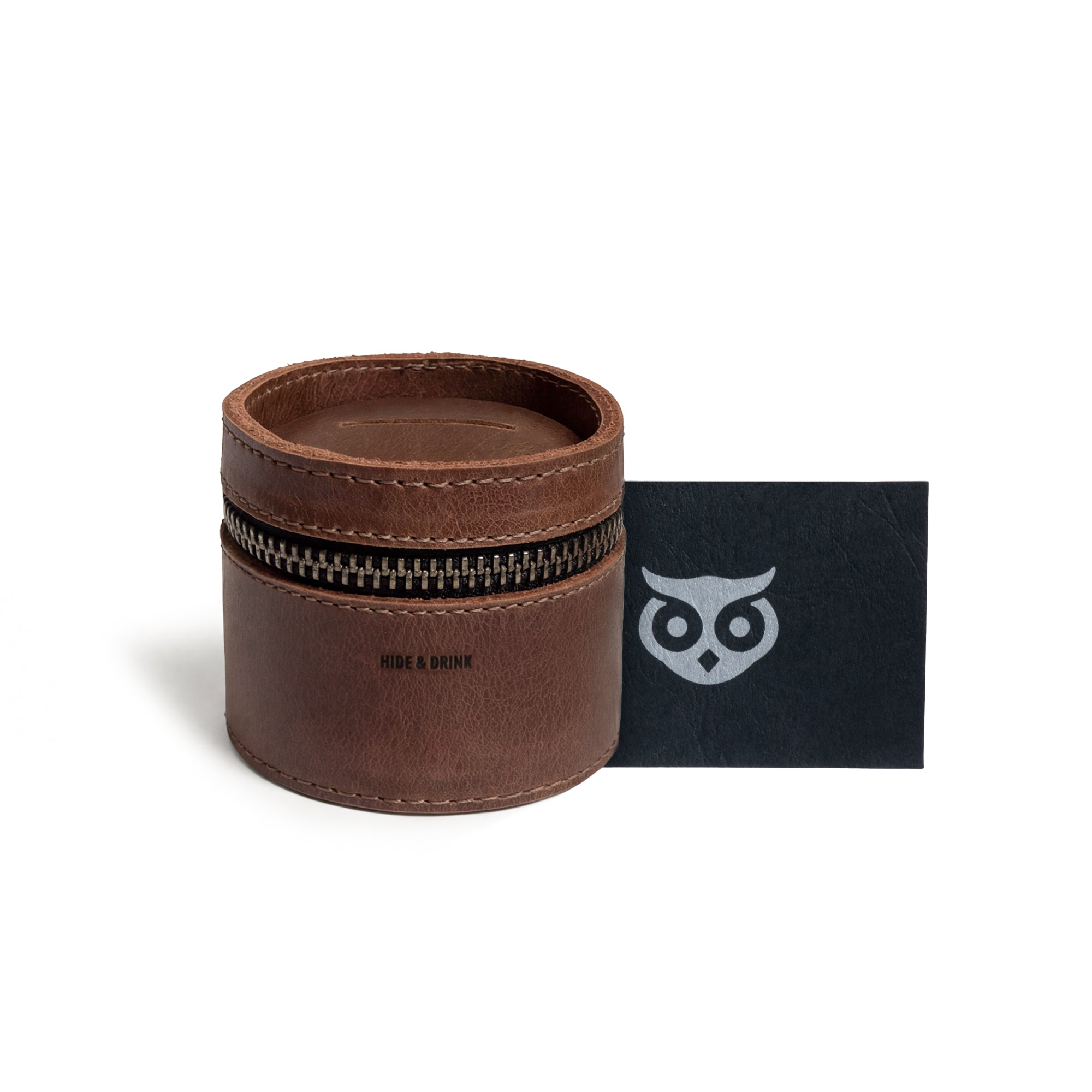 The Bucket Coin Release from Hide & Drink accompanied by a brand card, highlighting its status as a money box and piggy bank bucket. This full grain leather zippered pouch is an elegant cash organizer and coin case, showcasing artisan craftsmanship with hand-cut and hand-sewn techniques from La Antigua Guatemala & Oaxaca Mexico.