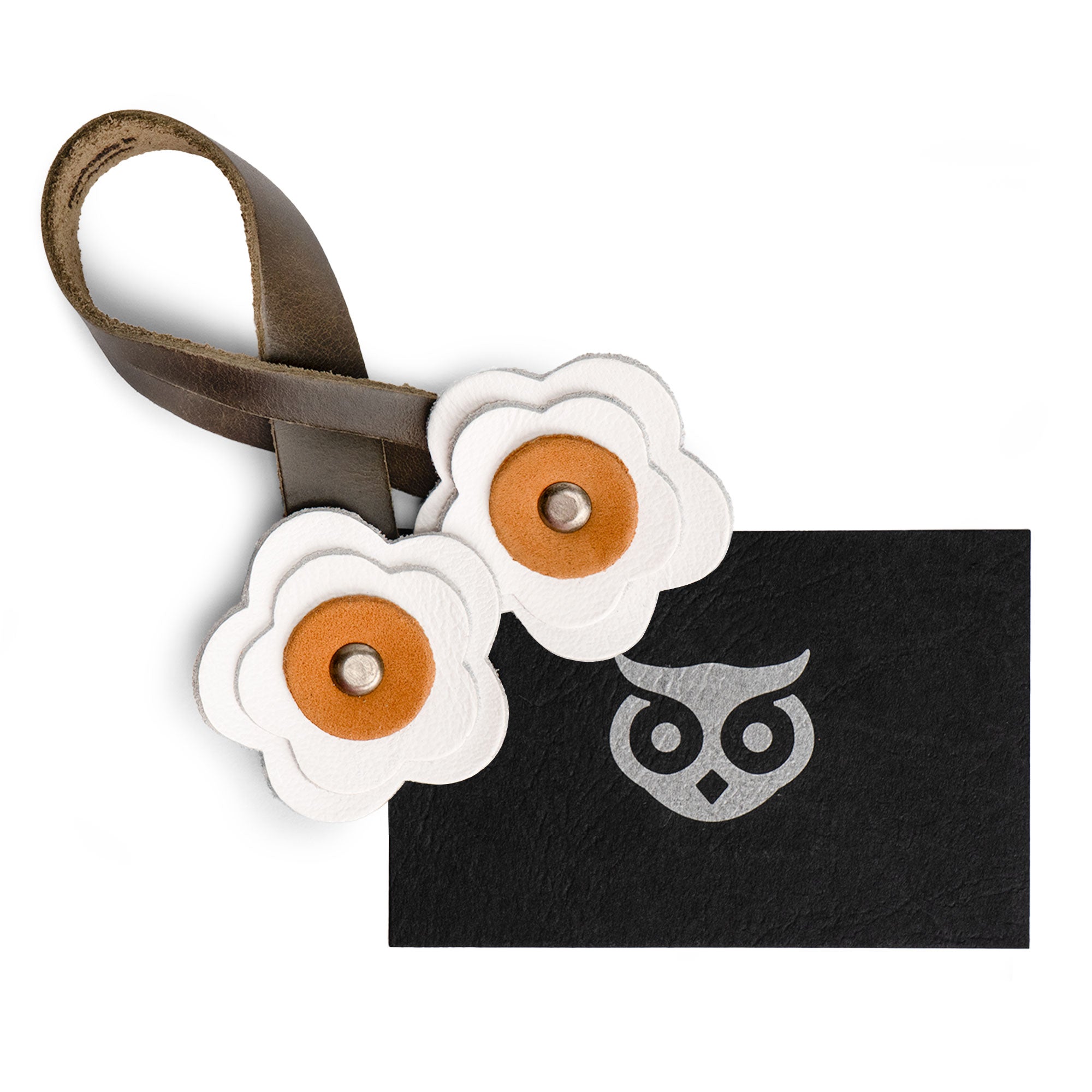 The Rose Bag Ornament by Hide & Drink next to a card, showcasing its vibrant colors and Full Grain Leather craftsmanship. This flower-shaped ornament is a charming accessory for stylish bags.