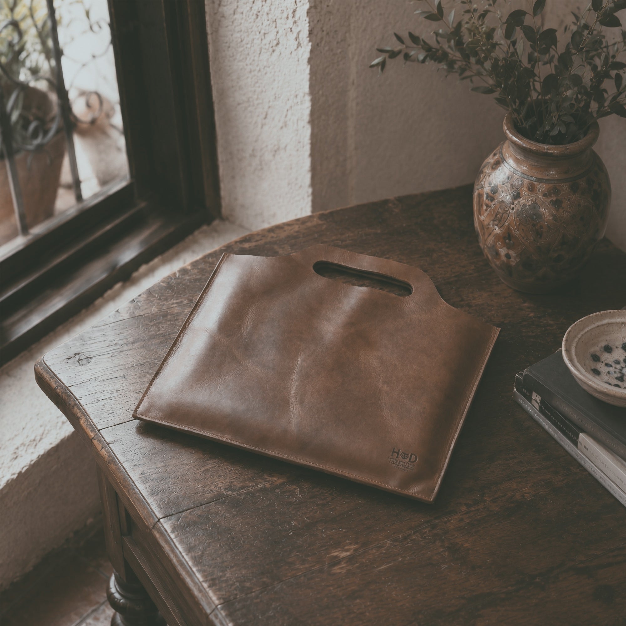 Flat Handbag by Hide & Drink featuring a smooth surface in dark brown full grain leather, ideal for a minimalist style carry-on bag or classic document holder. This thin portfolio showcases the beauty of small batch production, with each piece hand cut, hand sewn, and fire branded. Proudly handmade in La Antigua Guatemala & Oaxaca Mexico, it's a perfect travel accessory.