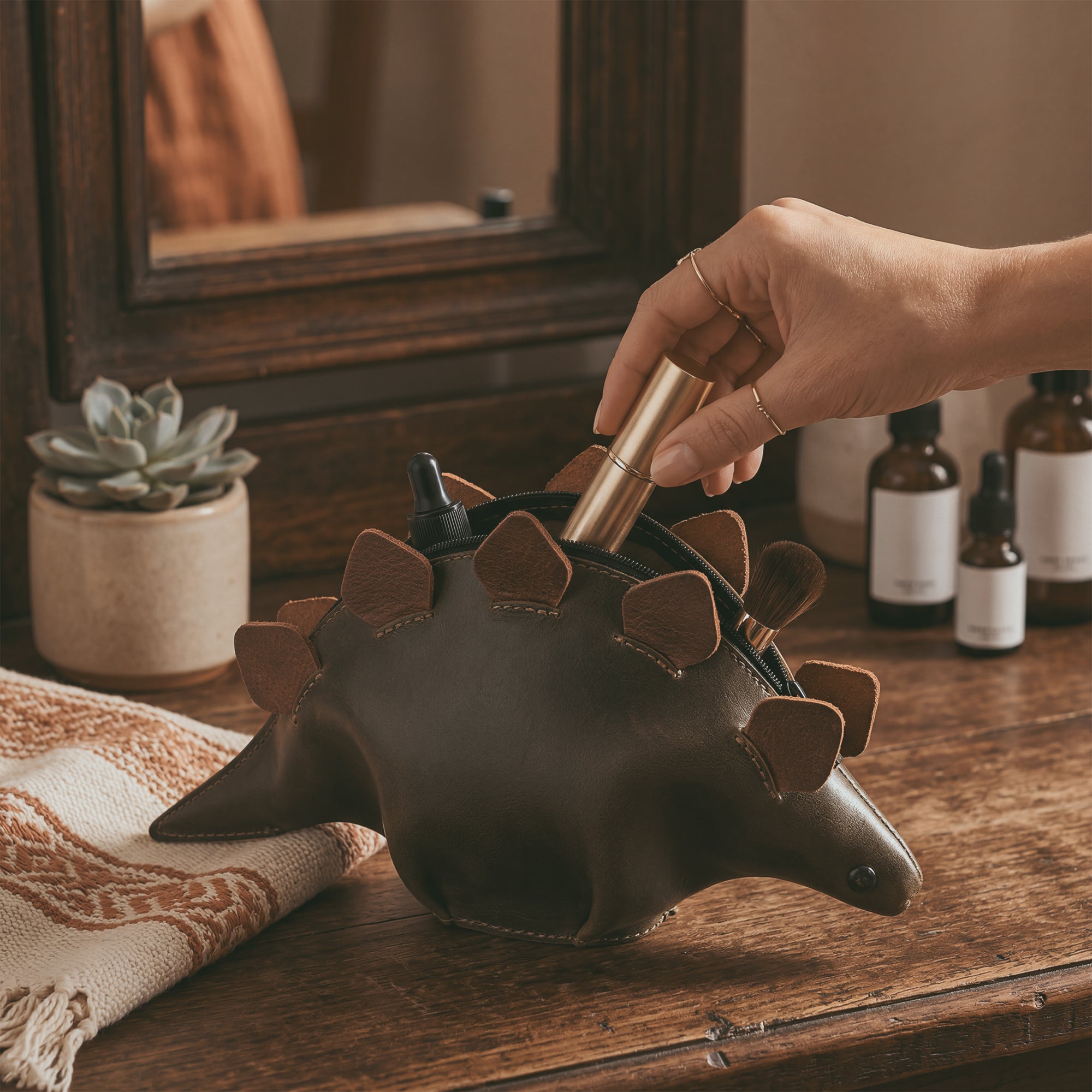 Lifestyle shot of the Leather Dinosaur Stegosaurus Pouch by Tudi Frudi, being used as a stylish accessory case. This artisan, dino-shaped pouch doubles as a cosmetic organizer and zippered cash holder wallet for coins, showcasing its handmade craftsmanship from La Antigua Guatemala and Oaxaca, Mexico.