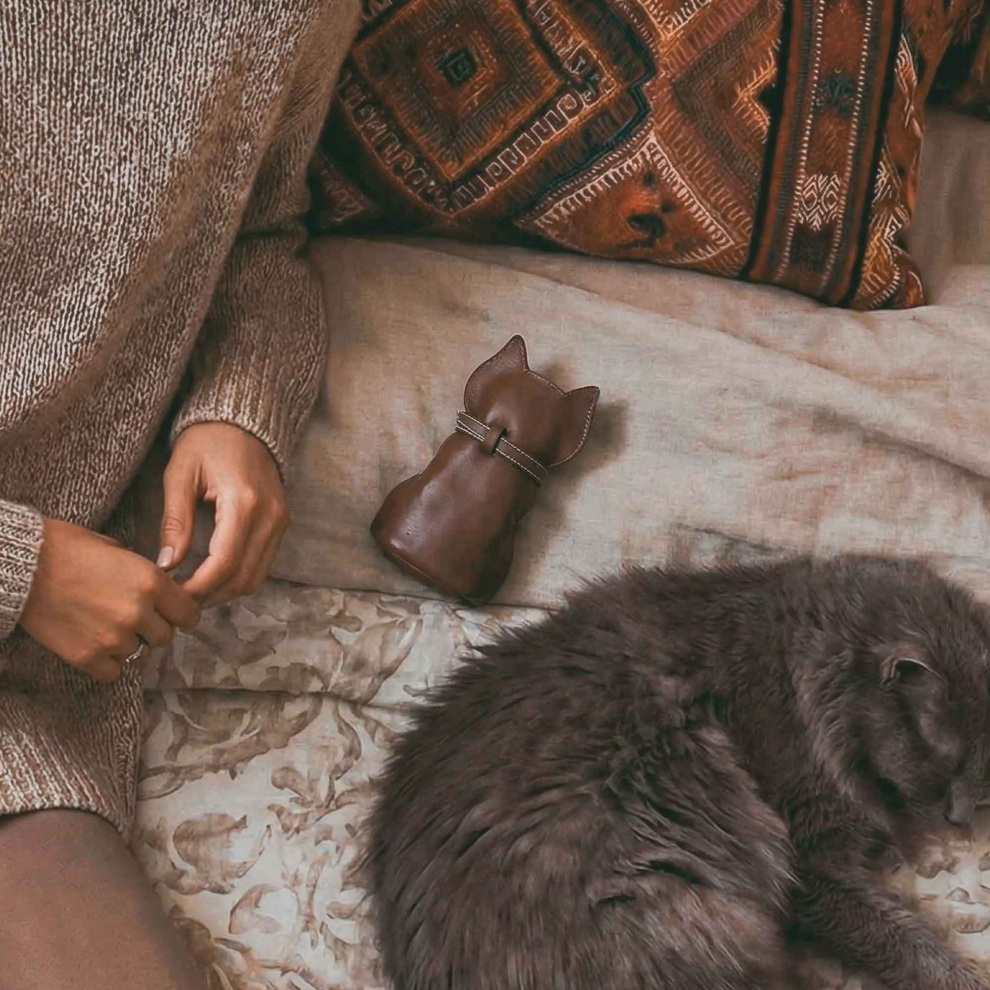 The Hide & Play Kitty Pouch nestled among cozy surroundings. This Full Grain Leather Small Coin Pouch doubles as a cute Change Purse, showcasing artisan craftsmanship from La Antigua Guatemala & Oaxaca Mexico, perfect for art lovers.