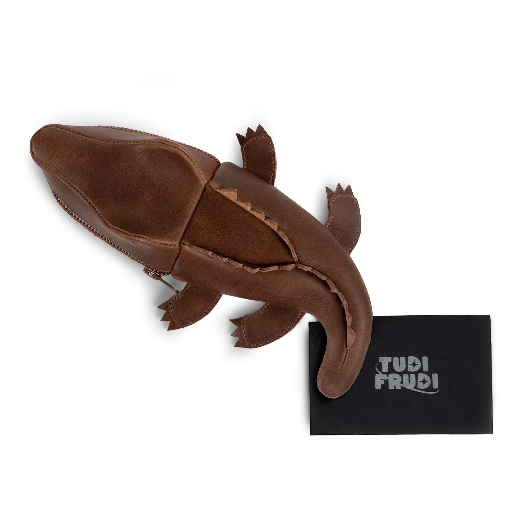 Leather Gator Pouch by Tudi Frudi presented with its packaging, highlighting the artisan details. This Gator Leather Pouch serves multiple functions, including as a crocodile-shaped pencil pouch or small charger cable holder. Made from full grain leather with a unique design, it's hand cut and sewn in small batch production, making it perfect for use as a change bag or scissors case. Handcrafted in La Antigua Guatemala & Oaxaca, Mexico, it embodies high-quality artisan craftsmanship.