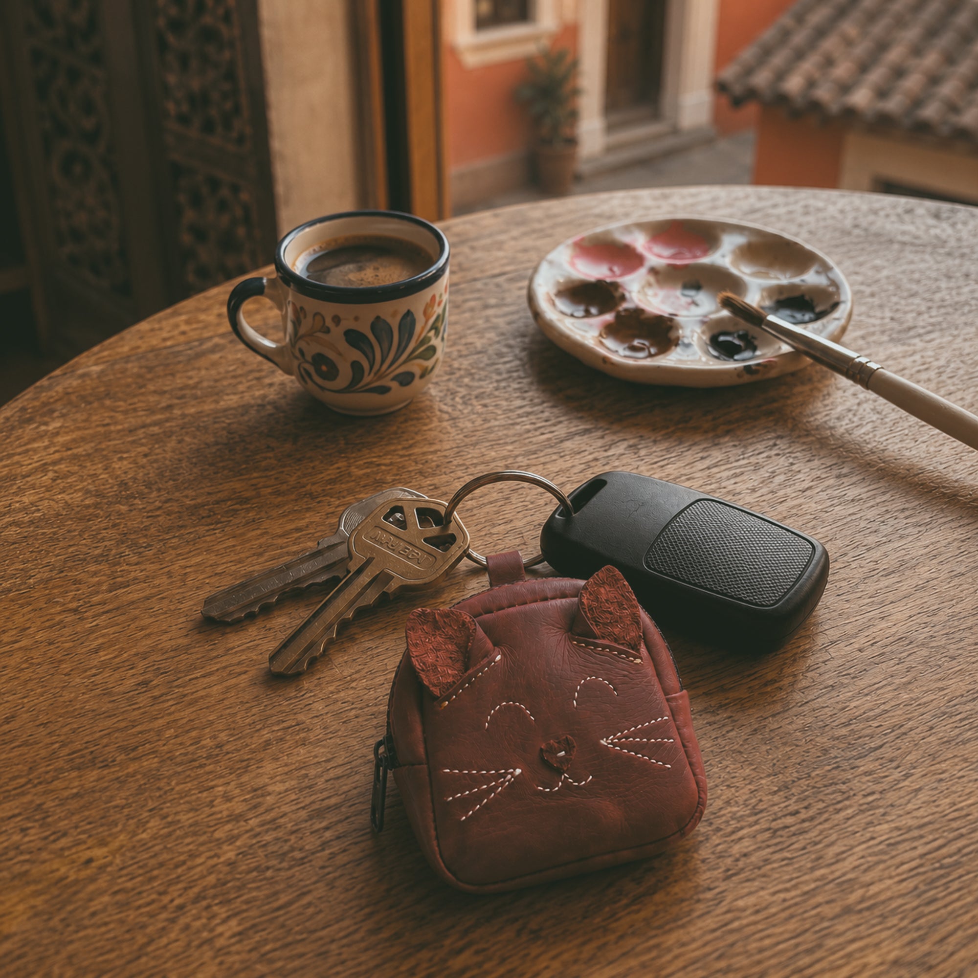 The Cheery Cat Mini Pack by Hide & Drink is featured alongside coffee and painting supplies, demonstrating its stylish functionality. This adorable mini backpack, made of Full Grain Leather, supports artisan craftsmanship from La Antigua Guatemala & Oaxaca, Mexico.