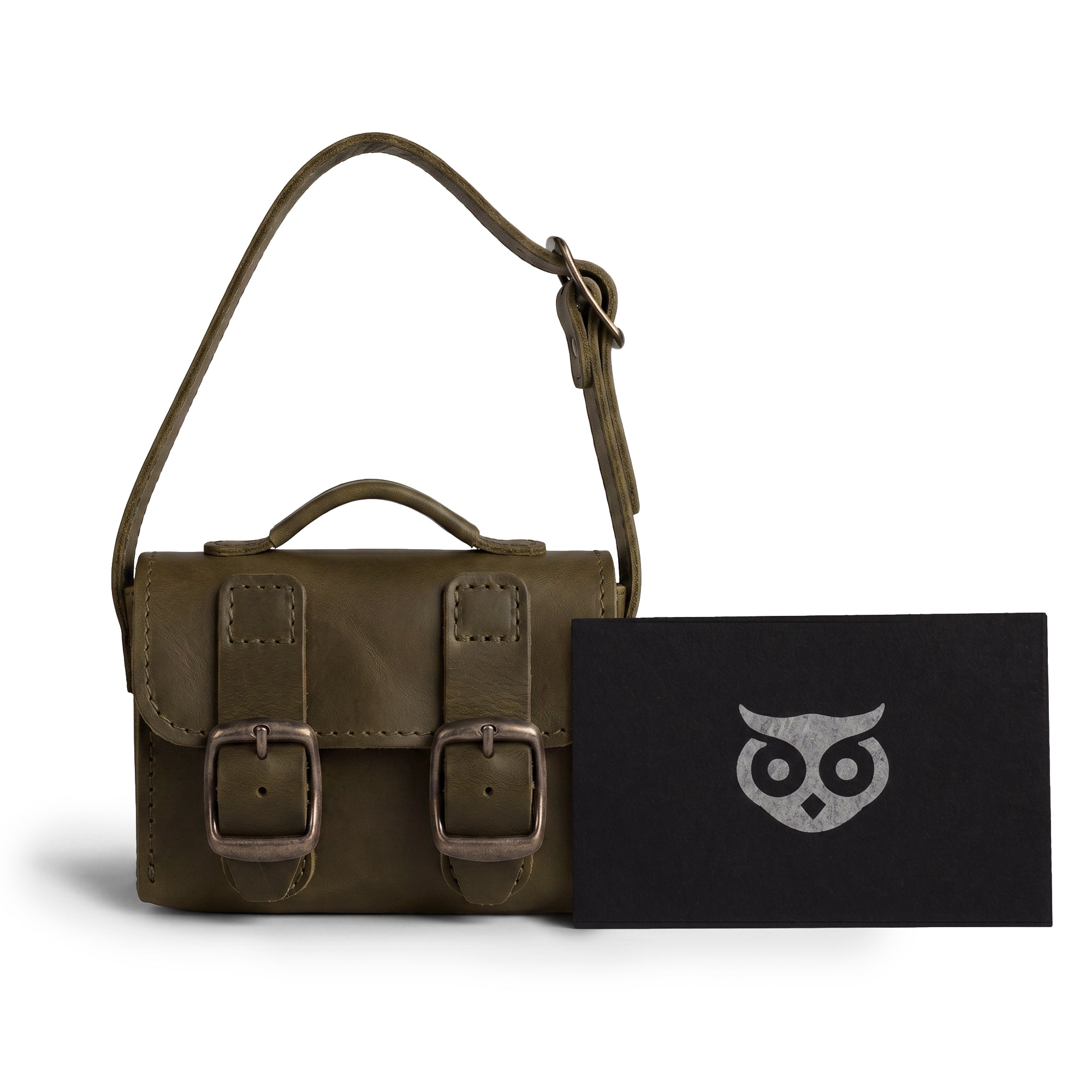 The green Tiny Messenger Bag by Hide & Drink, displayed with accompanying tags. This artisan Mini Messenger Bag Charm made from durable Full Grain Leather serves as both a keychain and handbag accessory, proudly made in La Antigua Guatemala.