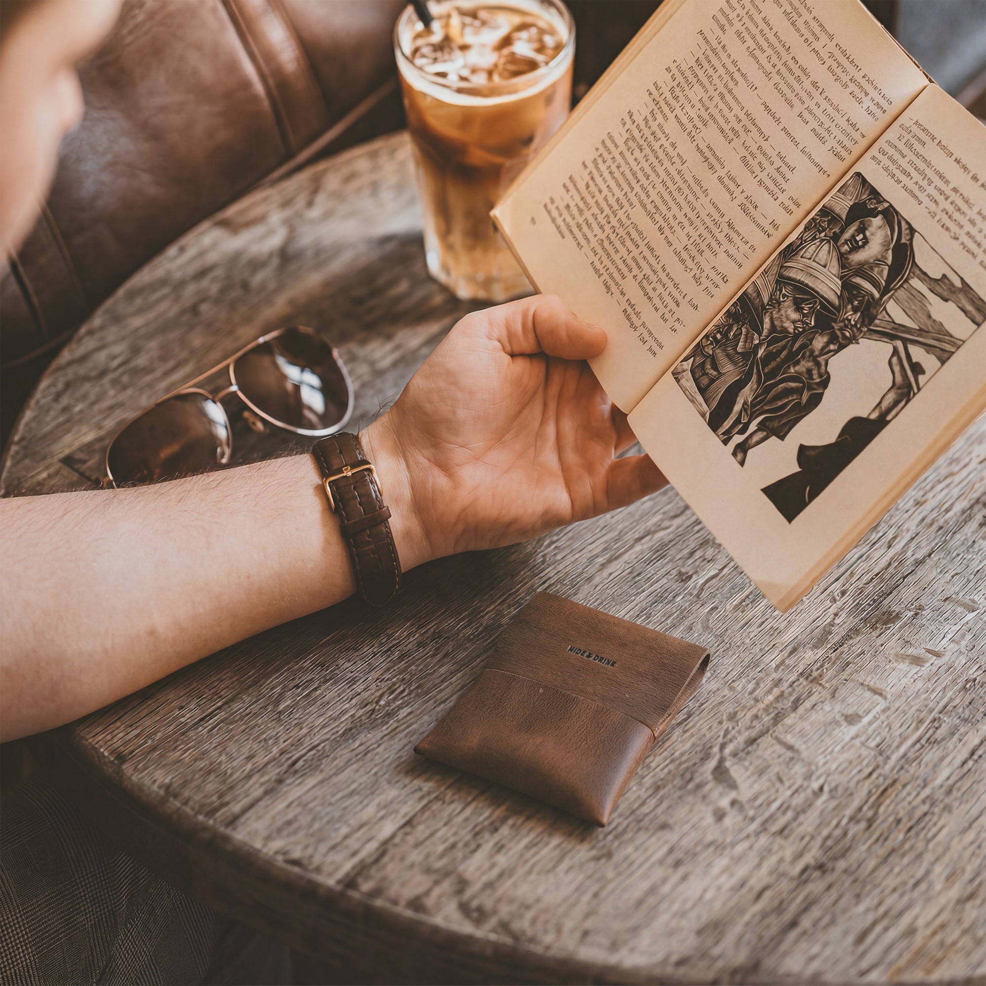 Aesthetic shot of a person relaxing with the Origami Card Wallet from Hide & Drink on a wooden table, highlighting its versatile design. This Leather Origami Card Holder serves as a Slim Wallet for Cards and Front Pocket Case for Debit & Credit Cards. Crafted with care in La Antigua Guatemala & Oaxaca Mexico, it embodies small batch production and artistry.