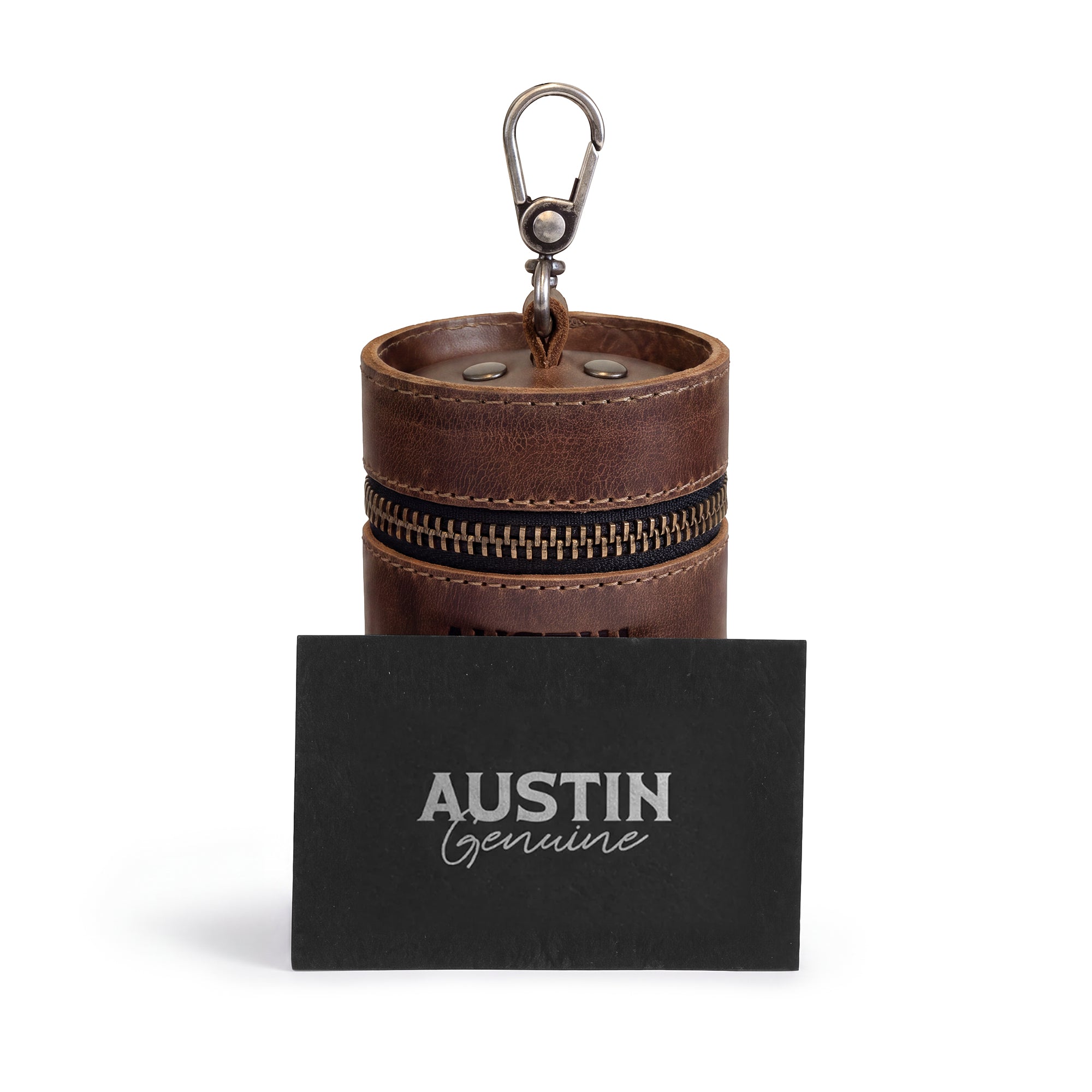 The Pease Mini Vanity Pouch by Austin Genuine, paired with a business card to emphasize its artisan branding. This unique cylinder for coins serves as a money box and piggy bank, crafted from full grain leather with attention to detail, adhering to small batch production standards, hand cut and hand sewn in La Antigua Guatemala & Oaxaca Mexico.