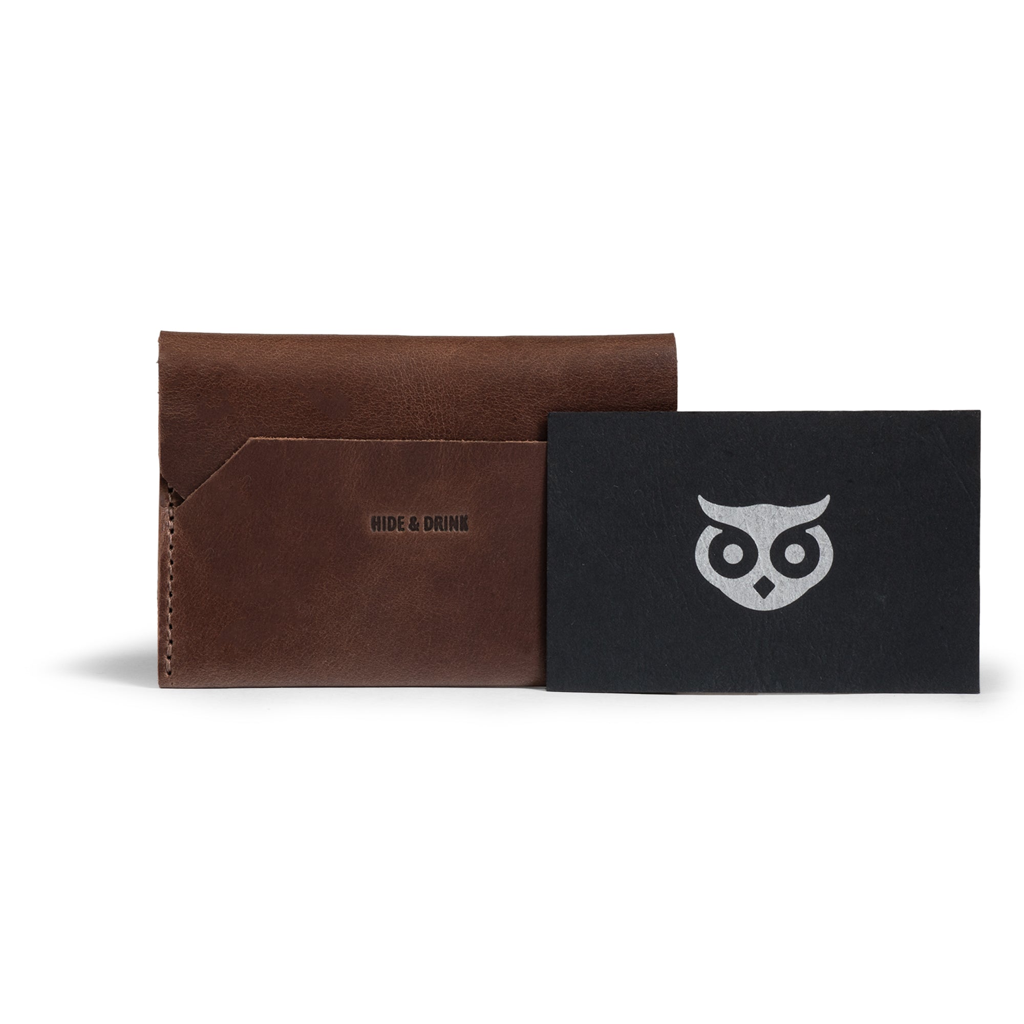 The Enfold Card Wallet by Hide & Drink displayed with a thank you card, highlighting its elegant leather card wallet design. This compact credit card holder for men also serves as a minimalist thin business card organizer with cash storage capabilities. Made from full grain leather, it showcases small batch production, hand cut and hand sewn craftsmanship, adorned with fire branding, representing the artisan skills from La Antigua Guatemala and Oaxaca Mexico.