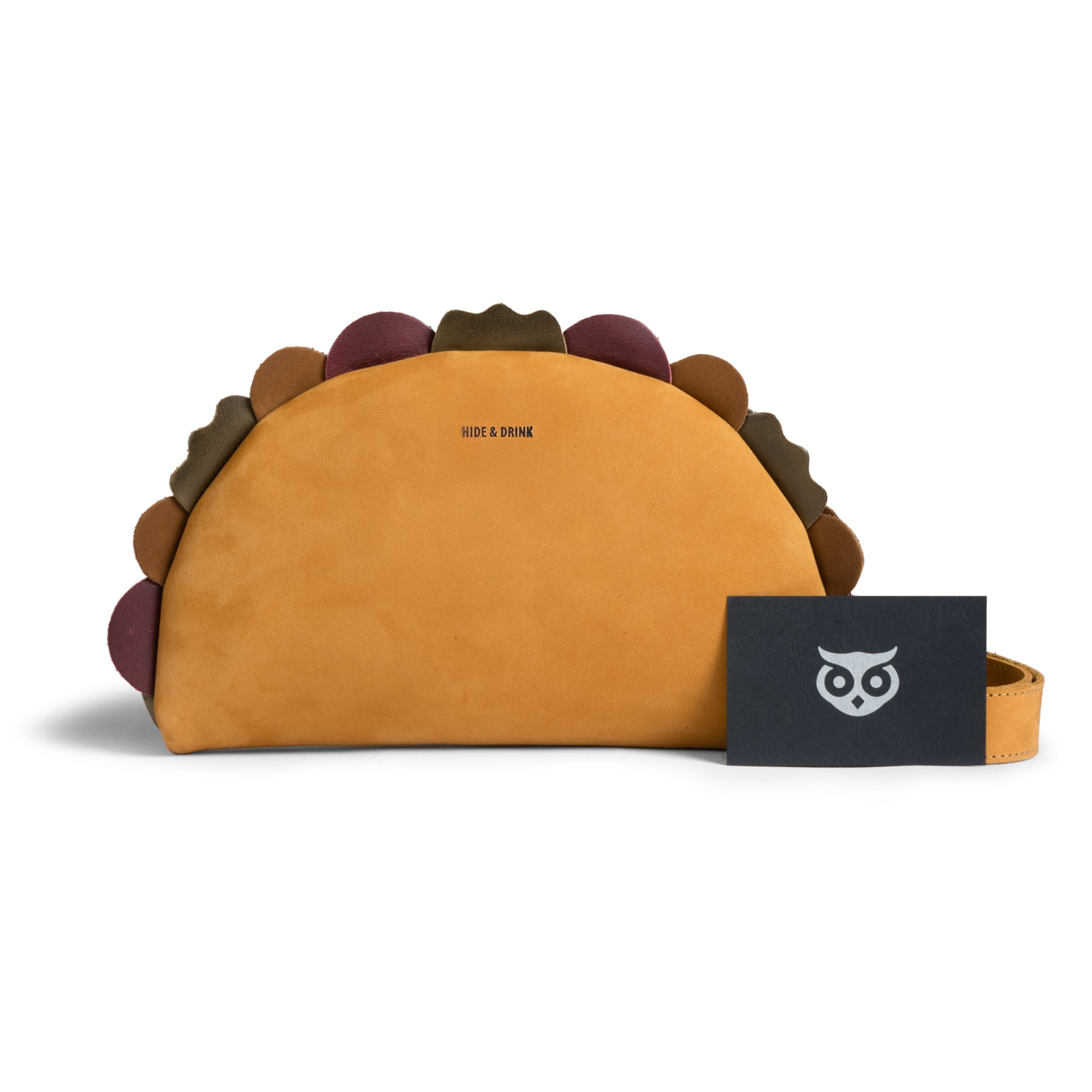 Showcasing the back view of the Taco-Shaped Crossbody Bag by Hide & Drink, complemented by branding details. This Leather Taco-Shaped Crossbody Bag with Adjustable Shoulder Strap epitomizes luxury and style, functioning as a satchel, messenger bag, or zippered sling bag. It's crafted from full grain leather, with each bag highlighted for its artisan quality from small batch production.