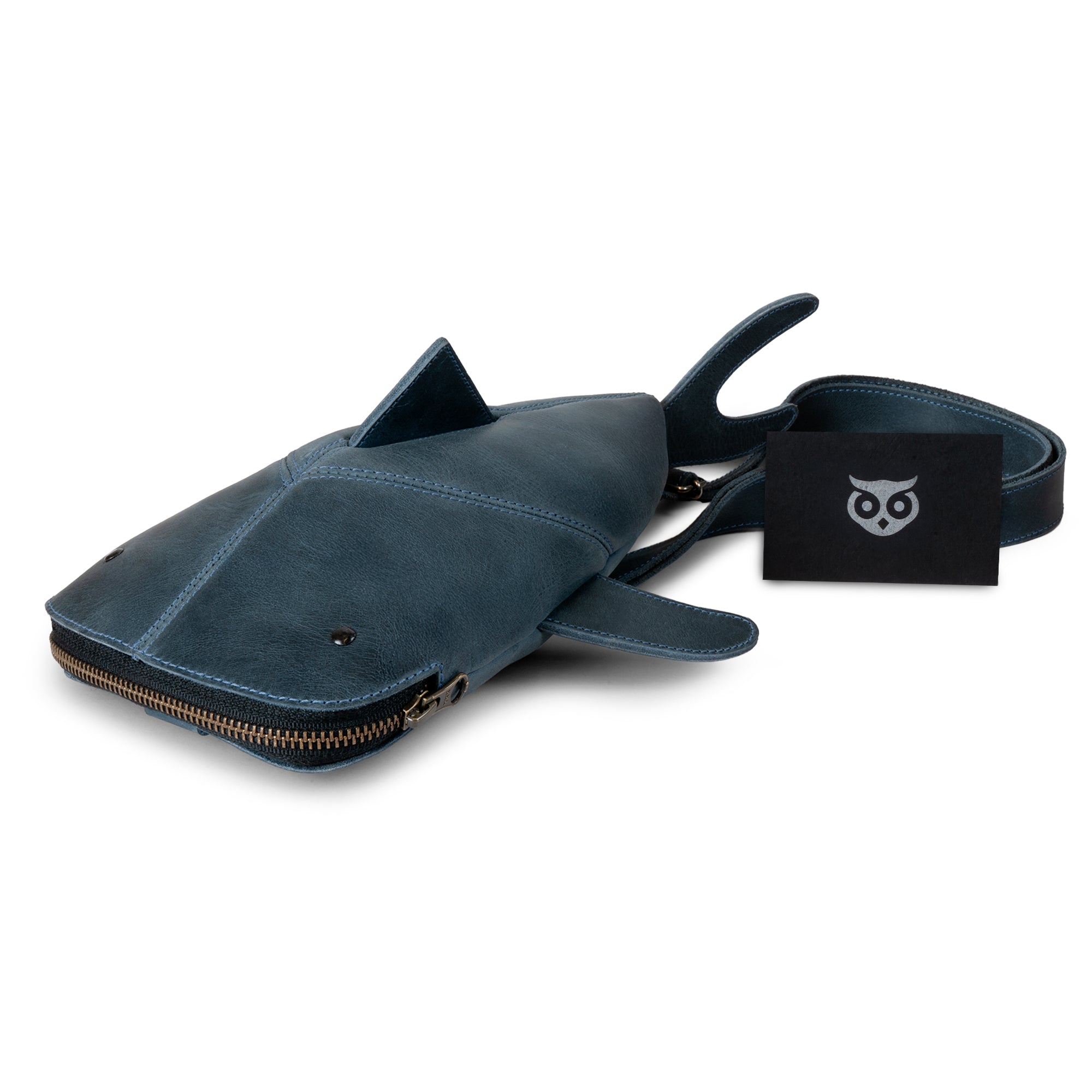 The Leather Shark Crossbody Bag by Hide & Drink, beautifully presented, highlighting its unique shark shape and gold zipper. This Leather Shark-Shaped Sling Bag is made from high-quality full grain leather and features an adjustable strap, making it an excellent choice for a messenger bag or shoulder bag. Handcut and sewn by artisans in La Antigua Guatemala & Oaxaca Mexico, it exemplifies quality craftsmanship.