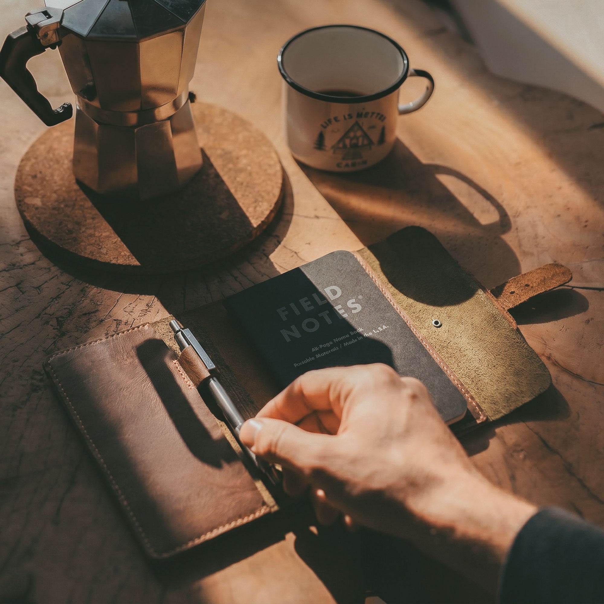 Hand holding the open Adventurer Field Notes Cover from Littlefield Chicago next to a coffee cup. This Adventurer Journal Cover for Field Notes (3.5 x 5.5 in. Notebook not Included) serves as an essential Notebook Holder and Journaling Accessory for Outdoors. Made from Full Grain Leather, it’s a refillable Travel Sleeve that reflects intricate hand cut and hand sewn methods by artisans in La Antigua Guatemala and Oaxaca Mexico.