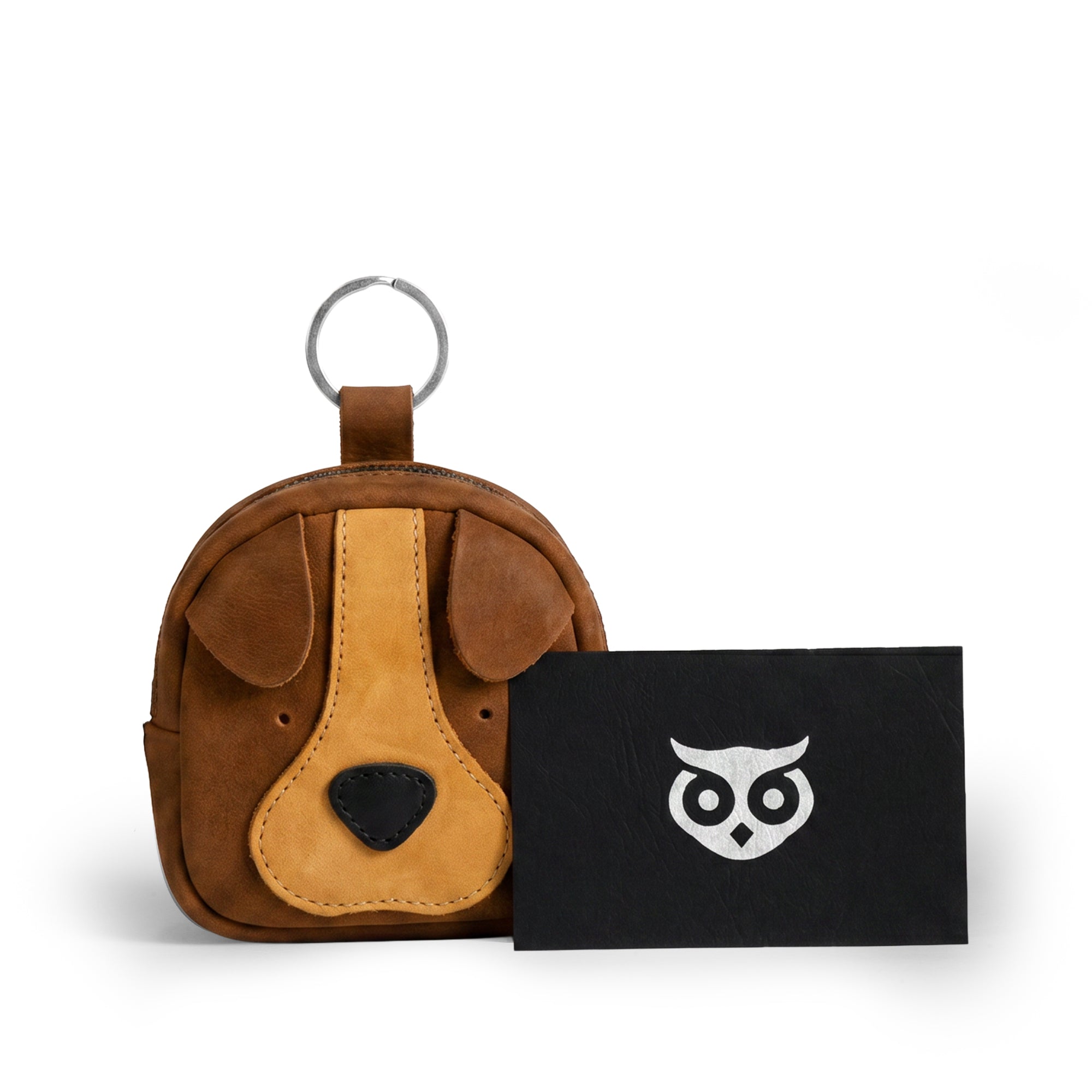 The Pouty Pup Mini Pack by Hide & Drink sits alongside a branded card, showcasing its charm and quality. This handmade suede leather mini purse serves as a stylish wallet or USB organizer, embodying artisan craftsmanship from La Antigua Guatemala.
