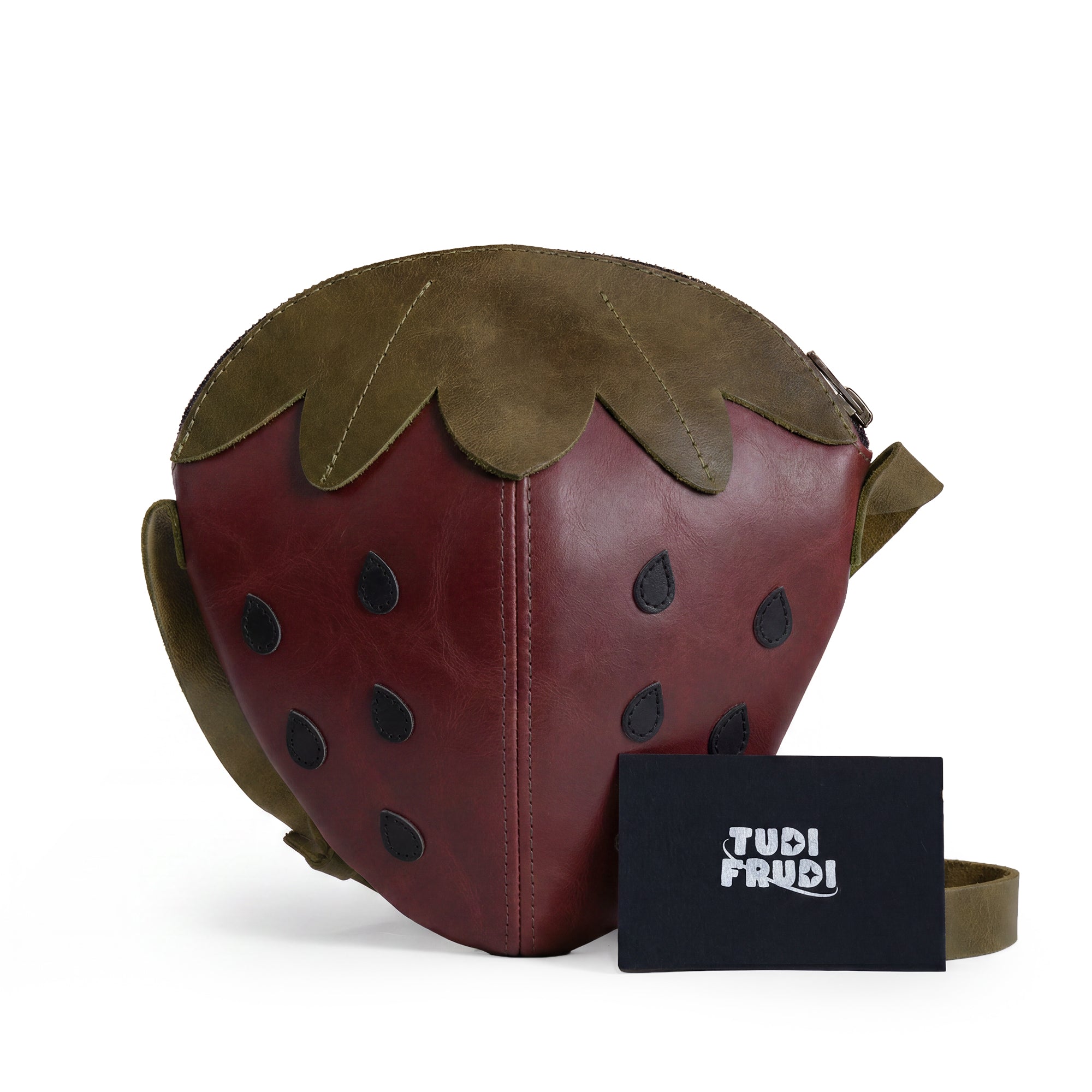 Finished Leather Strawberry-Shaped Shoulder Bag by Tudi Frudi with tags showcasing its artisanal roots. Made from Full Grain Leather, it illustrates the commitment to small batch production, hand-cut and hand-sewn craftsmanship, and is proudly handmade in La Antigua Guatemala & Oaxaca Mexico.