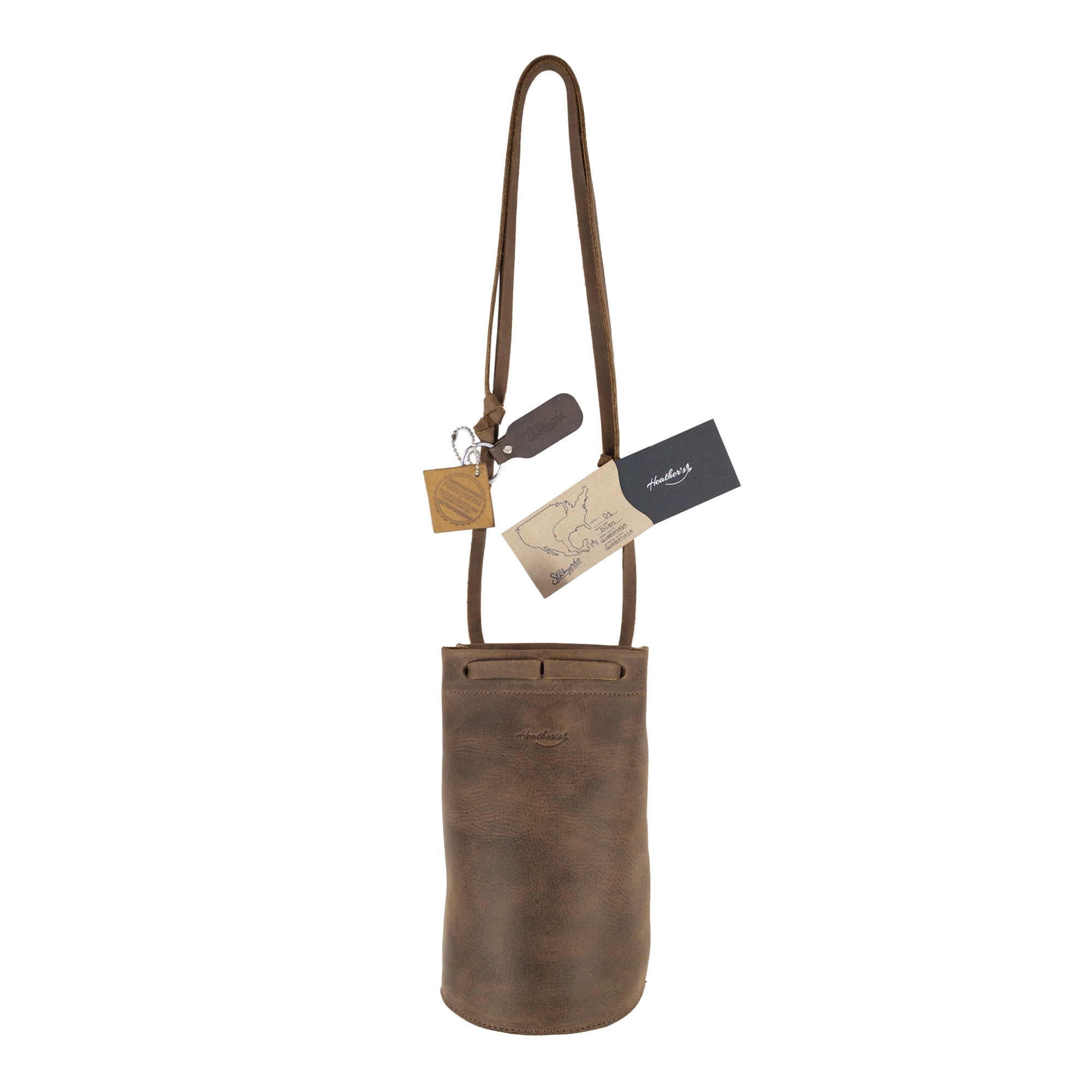 Heather's Cylinder Shoulder Phone Bag with tags and branding displayed, highlighting its artisan quality. This fashionable cylinder-shaped purse with adjustable shoulder strap is crafted from full grain leather, showcasing the artisan approach from StockyardX and reinforcing the values of small batch production and meticulous hand cut, hand sewn techniques. Handmade in La Antigua Guatemala & Oaxaca Mexico.