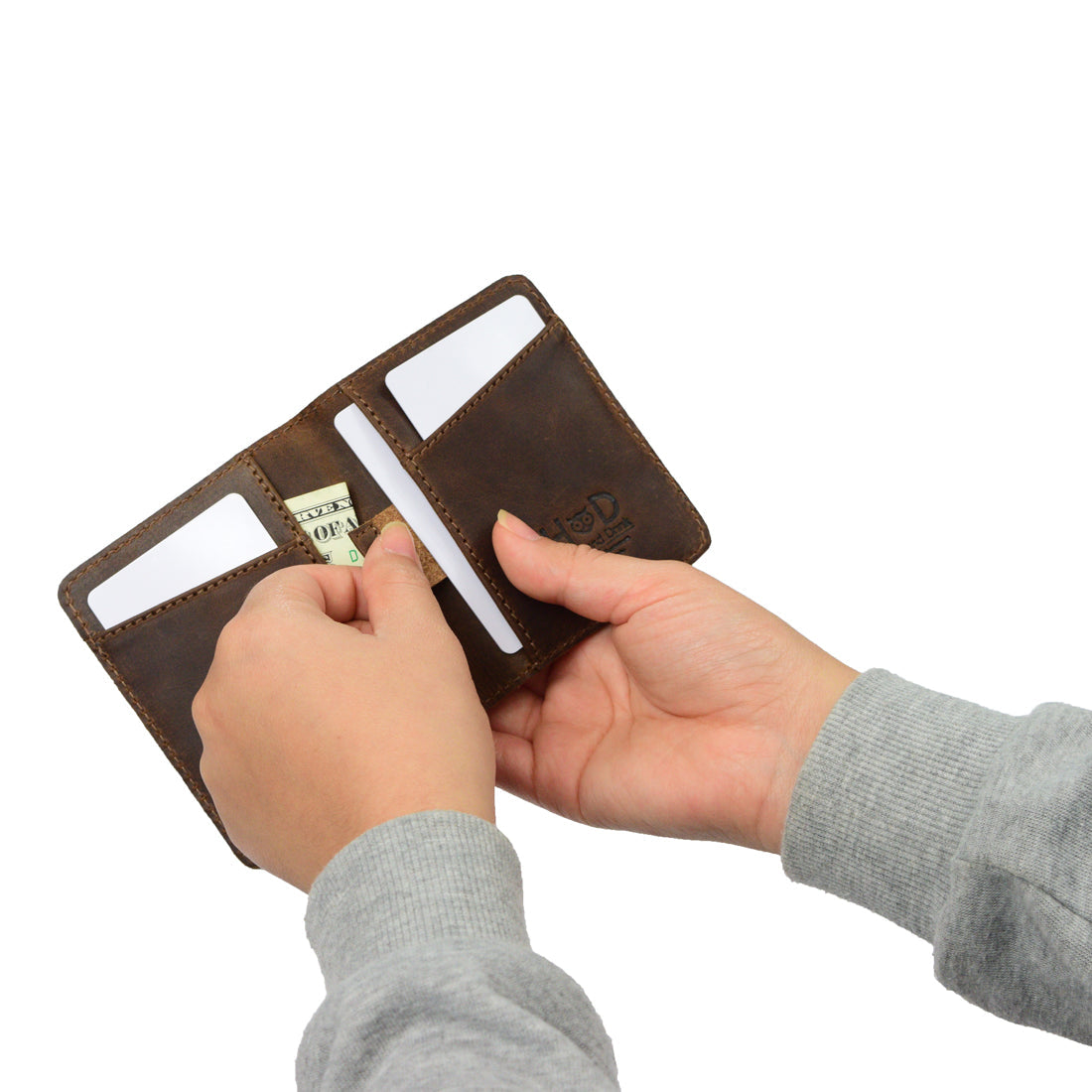 Person using Hide & Drink's Minimalist Bi-fold Wallet, placing cash inside. This handmade wallet in full grain leather represents everyday accessories, combining style and practicality as it holds up to 6 cards plus folded bills, crafted through small batch production in La Antigua Guatemala & Oaxaca Mexico.