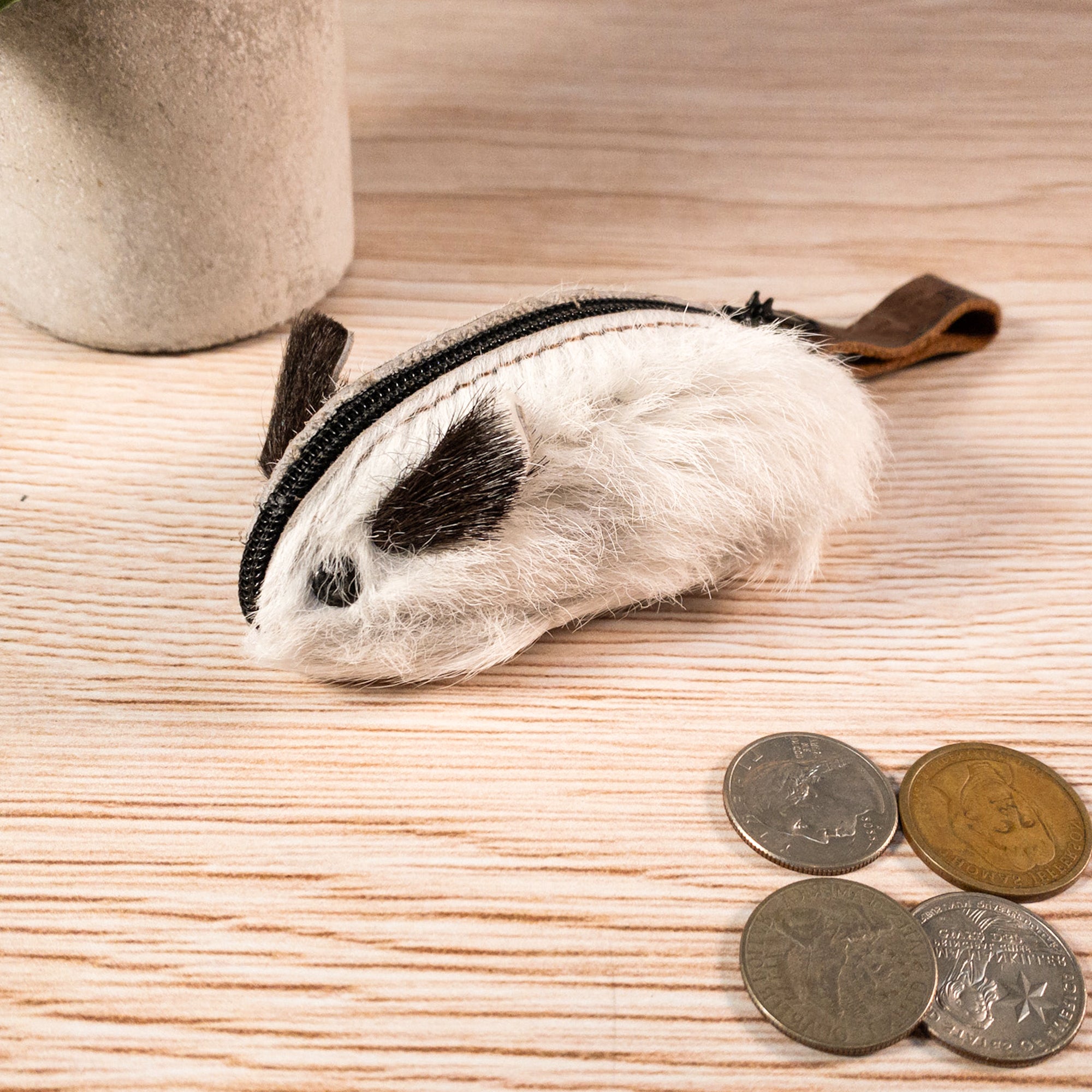 The Hide & Drink Mouse Coin Pouch filled with coins resting on a wooden table, displaying its functionality. This charming mouse-shaped change pouch is made from full grain leather and handcrafted in La Antigua Guatemala, serving as a practical and stylish travel accessory.