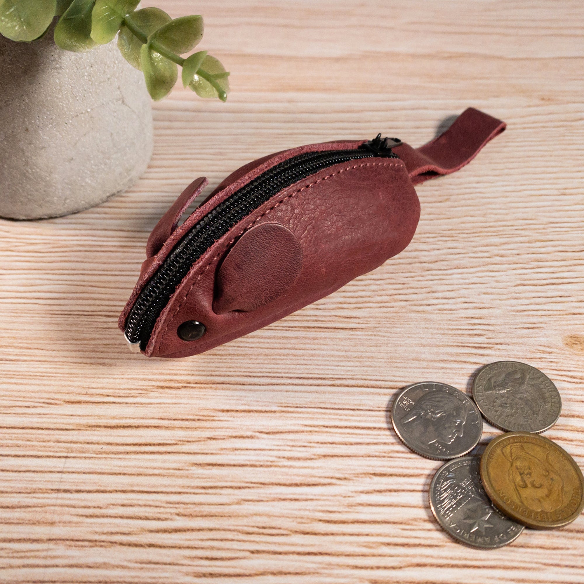 Casual setting featuring a brown Hide & Drink's Mouse Coin Pouch alongside loose change. This handcrafted Mouse-Shaped Coin Pouch embodies artisan quality and serves as a playful yet functional travel accessory.