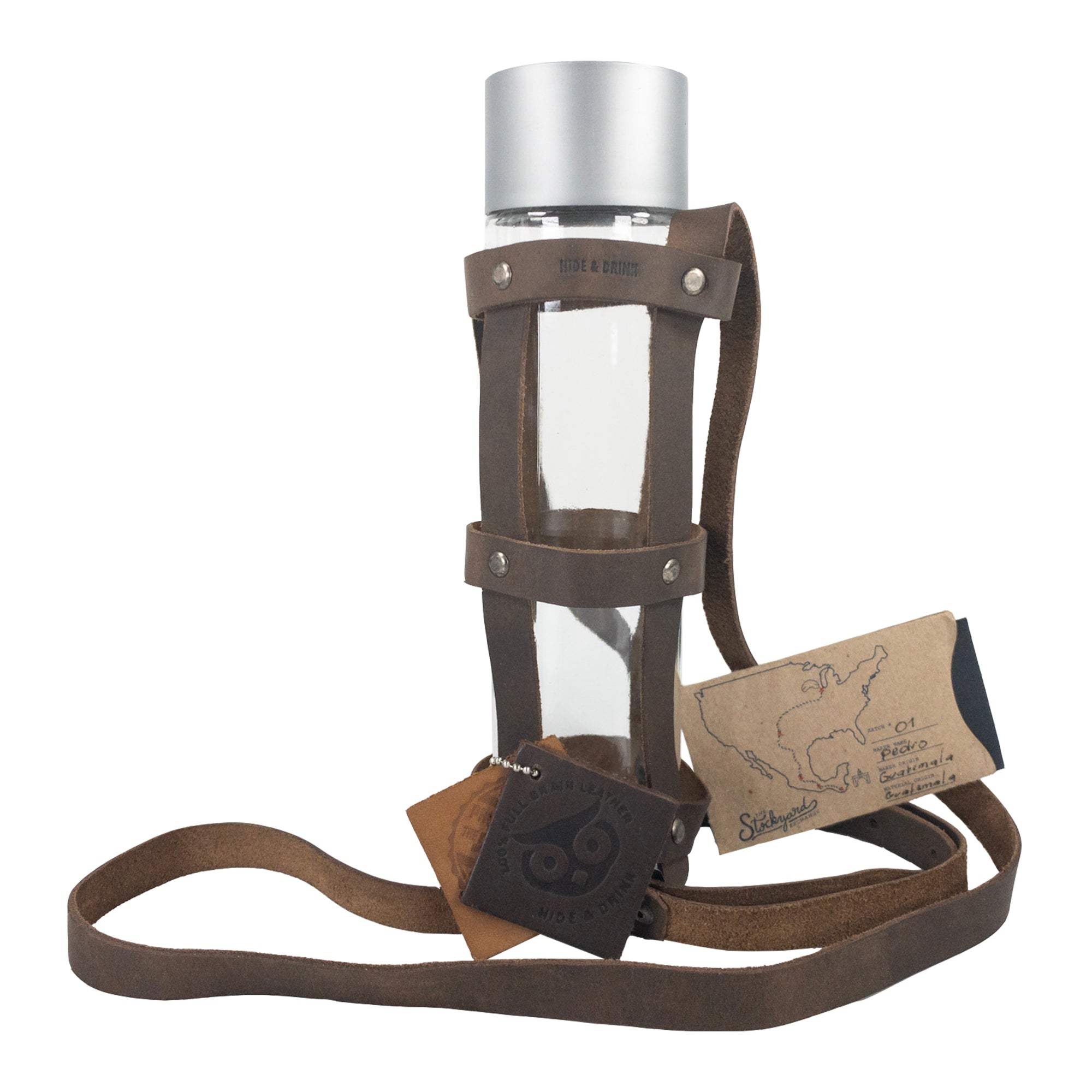 The Hide & Drink Riveted Bottle Carrier (Bottle Included) with accompanying packaging, showcasing the product and its artisan connection. This full grain leather travel accessory represents the essence of small batch production and artisan craftsmanship with hand cut, hand sewn, and fire branded detailing, made in La Antigua Guatemala & Oaxaca Mexico.