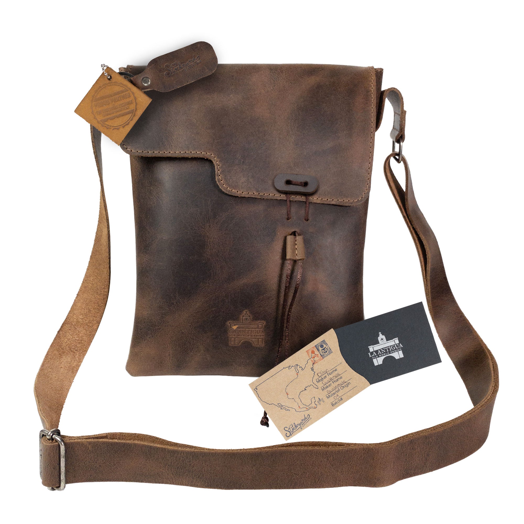La Antigua Treasure Crossbody Bag displayed alongside its artisan tags, illustrating its handmade nature and vintage design. Made from rustic full grain leather, this small batch production accessory is a perfect blend of style and functionality, handcrafted in La Antigua Guatemala.