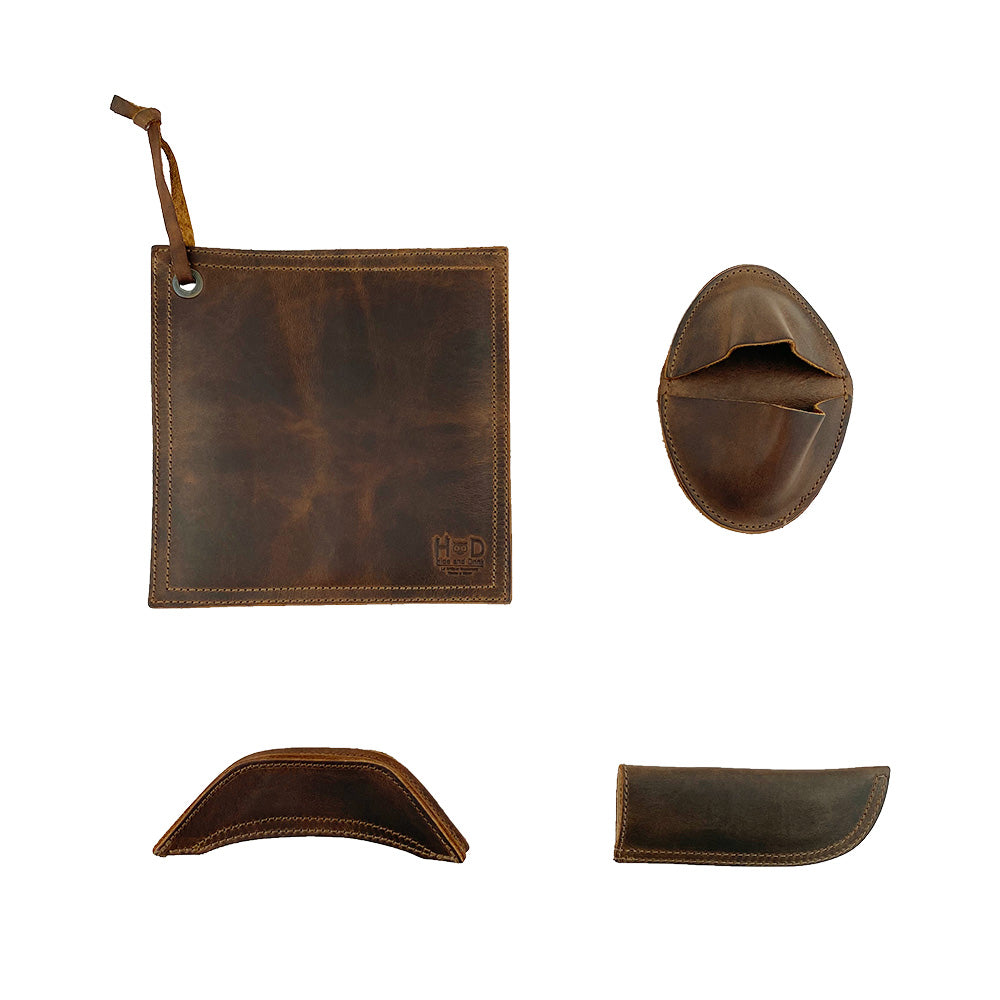 Hide & Drink Hot Handle Holders (Set of 4) display a combination of essential kitchen tools including a Panhandle and Side Kick, plus a Grip Mitt and Square Pot Holder, all made from robust Full Grain Leather. This artisan product, made through small batch production, is hand cut and hand sewn, providing durability and style, handmade in La Antigua Guatemala & Oaxaca Mexico.