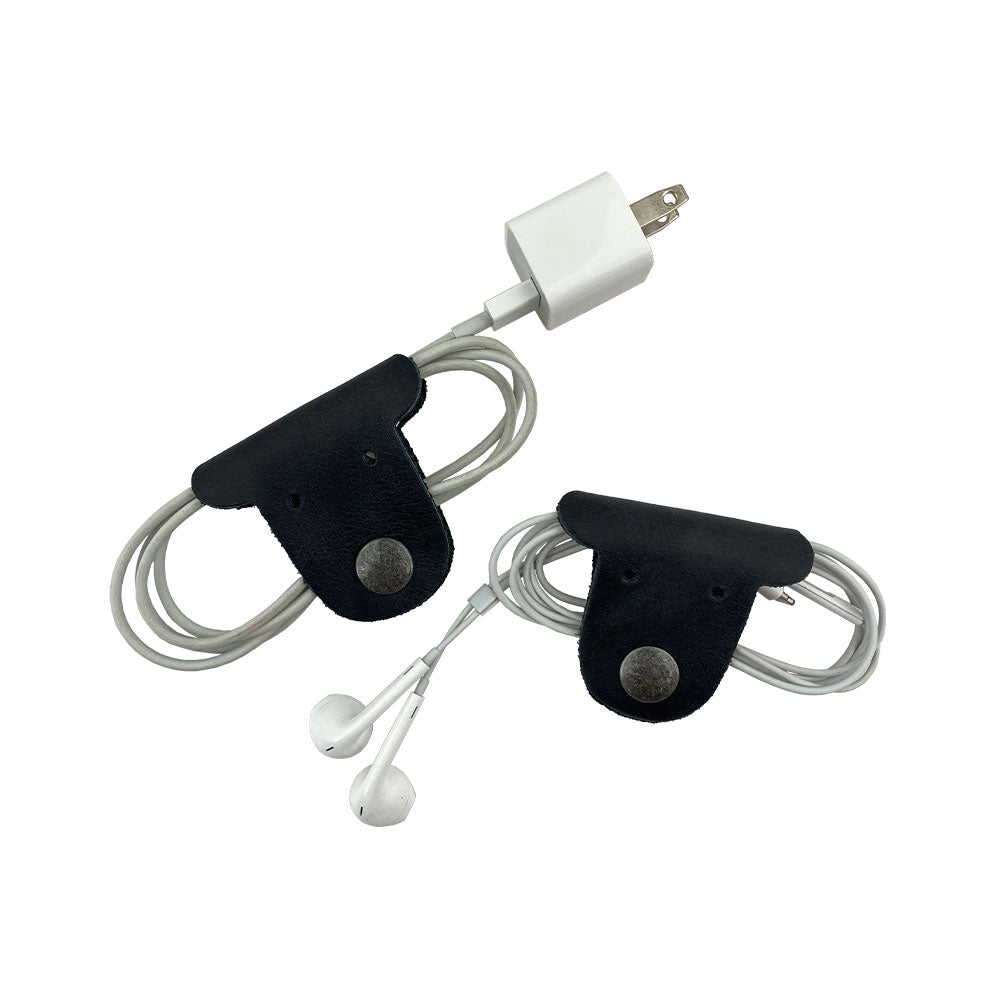 Two black Dog Shaped Cord Keepers organizing earbuds with stylish flair, a smart design from Hide & Drink made from Full Grain Leather. Dog Shaped Cord Keeper (Cord Clam) 2-Pack, Full Grain Leather, StockyardX, Small Batch Production, Hand Cut, Hand Sewn, Fire Branded, Artisan, Handmade in La Antigua Guatemala & Oaxaca Mexico.