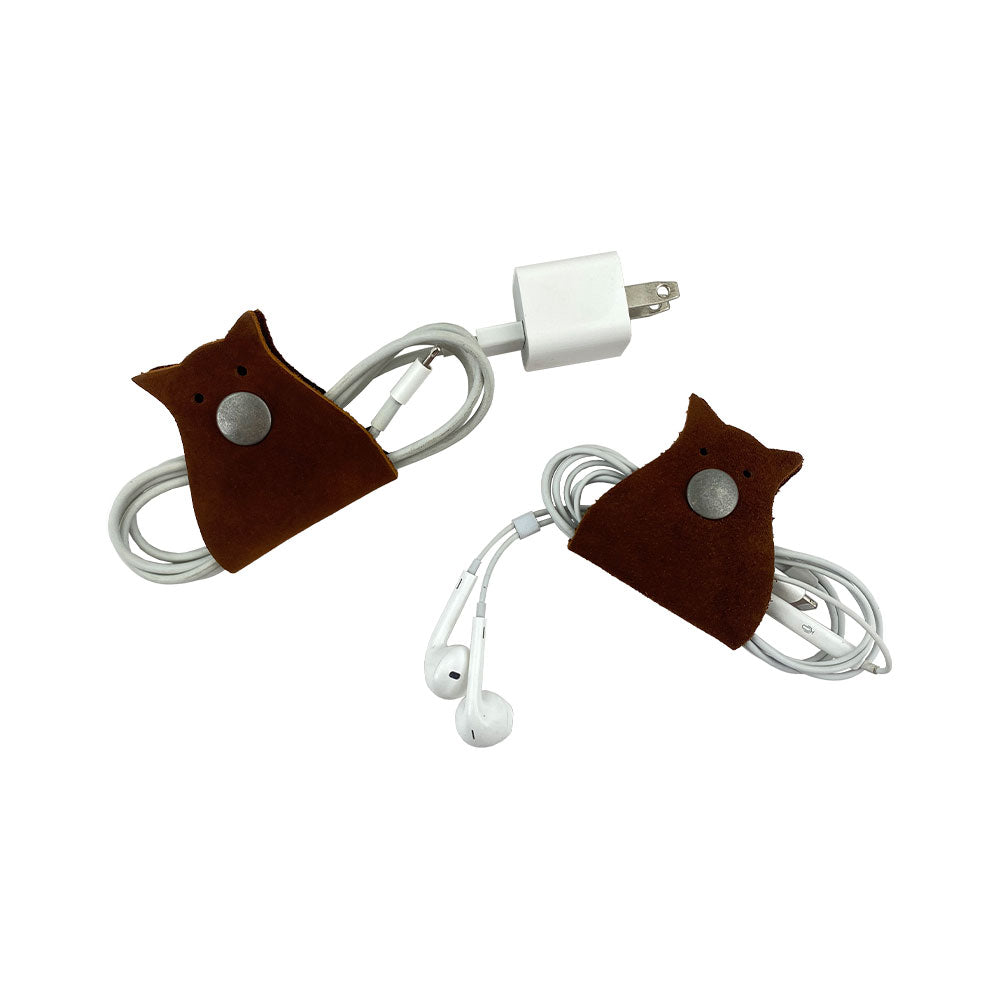 Owl Shaped Cord Keeper (2-Pack) by Hide & Drink presented with earphones and a charging cable wrapped neatly in stylish leather organizers. Owl Shaped Cord Keeper (Cord Clam) 2-Pack. Full Grain Leather, StockyardX, Small Batch Production, Hand Cut, Hand Sewn, Fire Branded, Artisan, Handmade in La Antigua Guatemala & Oaxaca Mexico.
