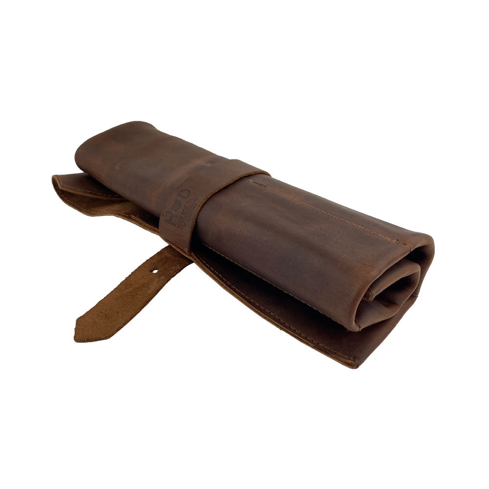 A rolled-up Large Tool Roll by Hide & Drink, perfect for storing various tools. This Portable Carry-On Pouch includes 6 slots for woodworking tools organization. Made from premium waxed canvas and full grain leather variations, this handmade item showcases artisan craftsmanship, featuring hand-cut, hand-sewn elements in La Antigua Guatemala & Oaxaca Mexico.