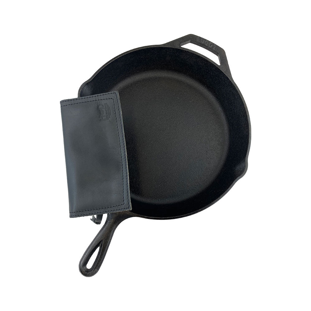 Hide & Drink Pot Pad placed alongside a cast iron skillet, showcasing its functionality as a hot pad. Made from quality full grain leather, it features a double-layered design.