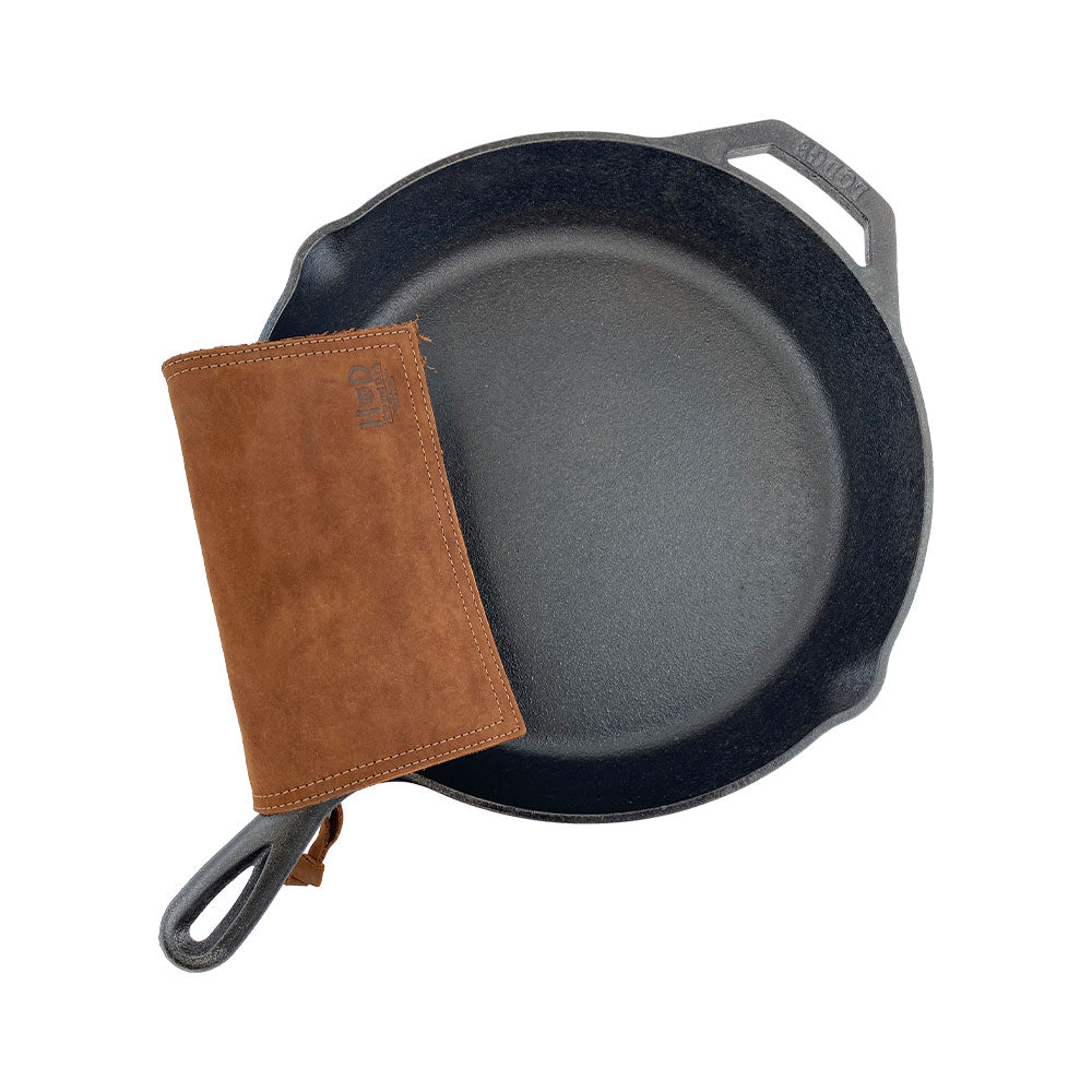 Hide & Drink Pot Pad elegantly placed next to a cast iron skillet, illustrating its role as a hot pot pad. Crafted with rustic leather, it's double-layered for extreme durability. Handmade in La Antigua Guatemala & Oaxaca Mexico.