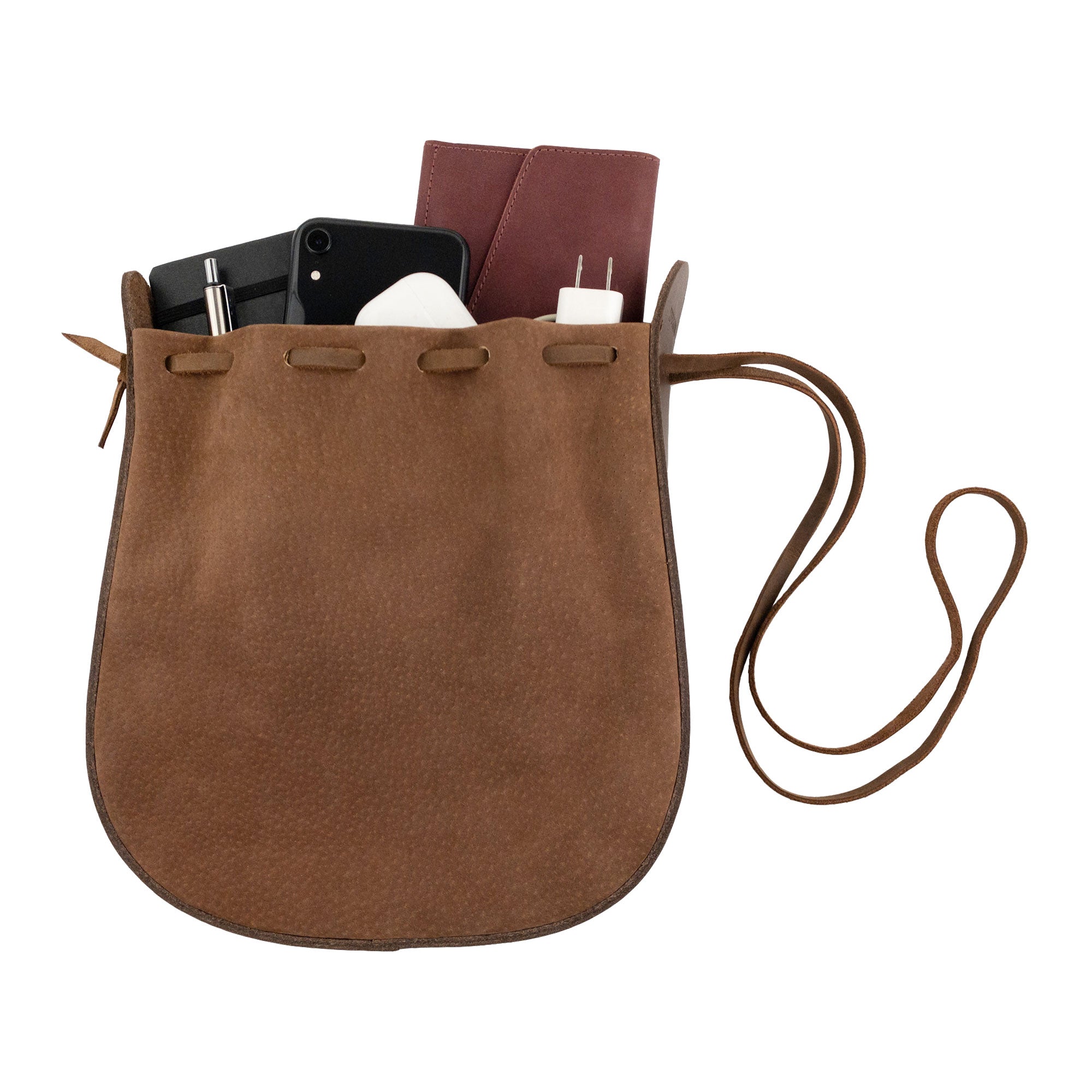 Heather's Shoulder Bag partially filled with essentials, illustrating its functionality as a multipurpose rounded shoulder bag. Crafted from full grain leather, this travel-friendly bag embodies artisan craftsmanship through small batch production, hand cut and hand sewn details, and is fire branded. Handmade in La Antigua Guatemala & Oaxaca Mexico.