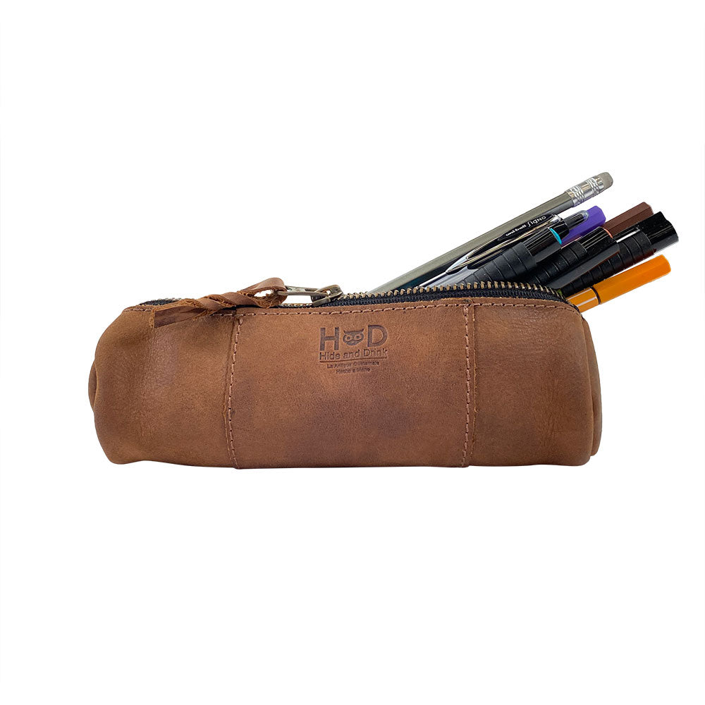 Utility Cylinder Case by Hide & Drink shown with pens, ideal for organizing stationery or personal items. This classic bag is handmade from Full Grain Leather, crafted in small batches in La Antigua Guatemala. Cylinder Case, Handmade, Rustic.