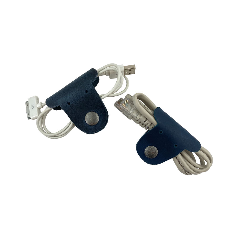 Two navy blue Dog Shaped Cord Keepers neatly managing USB cables, an innovative way to keep cords tidy by Hide & Drink, made from Full Grain Leather. Dog Shaped Cord Keeper (Cord Clam) 2-Pack, Full Grain Leather, StockyardX, Small Batch Production, Hand Cut, Hand Sewn, Fire Branded, Artisan, Handmade in La Antigua Guatemala & Oaxaca Mexico.