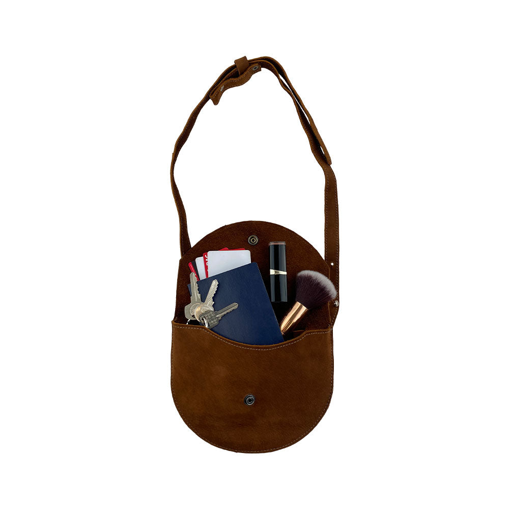 The light tan Hide & Drink Hip and Shoulder Bag filled with items, showcasing its practical design and Full Grain Leather quality. This bag reflects Small Batch Production, with its hand cut, hand sewn, and fire branded elements. Handmade in La Antigua Guatemala & Oaxaca Mexico.