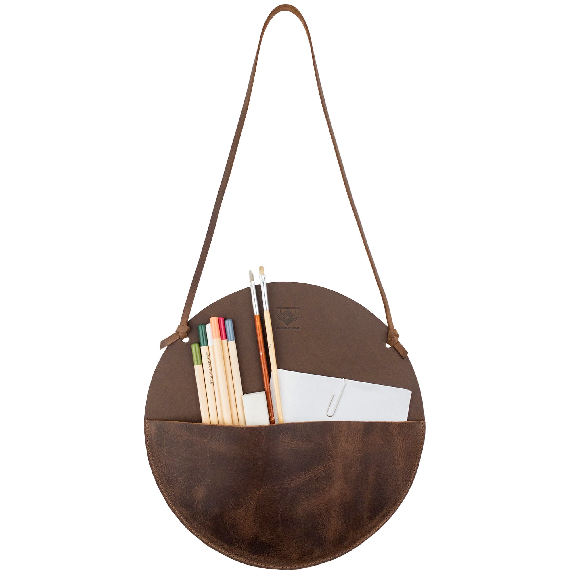 Stylish Leather At Home Circular Wall Hanger showcasing pens, colored pencils, and a notepad. This leather wall file organizer is ideal for storing various items, emphasizing handmade quality and artisan design from La Antigua Guatemala.